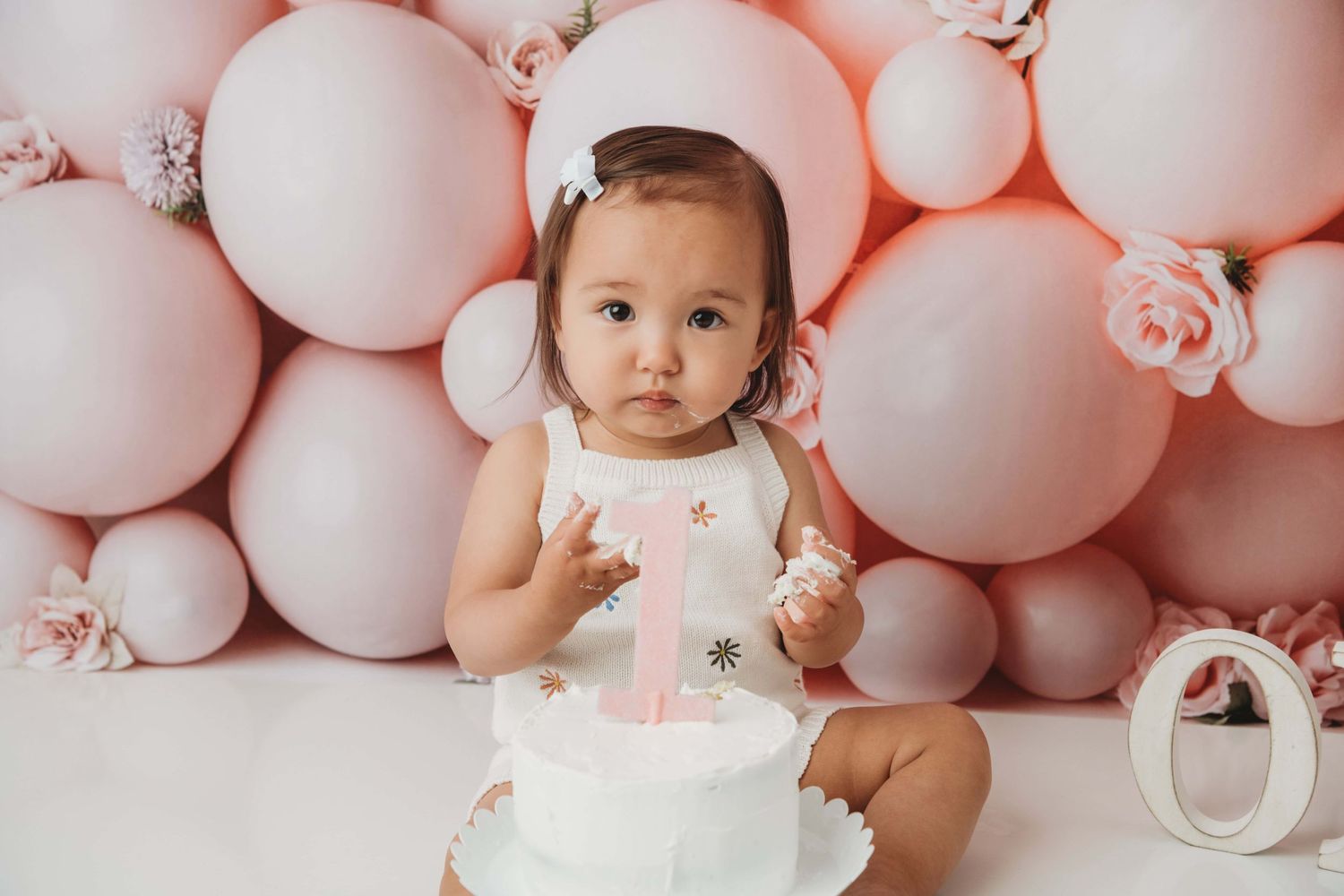 A one year old girl eats her white cake with a pink cake topper.
