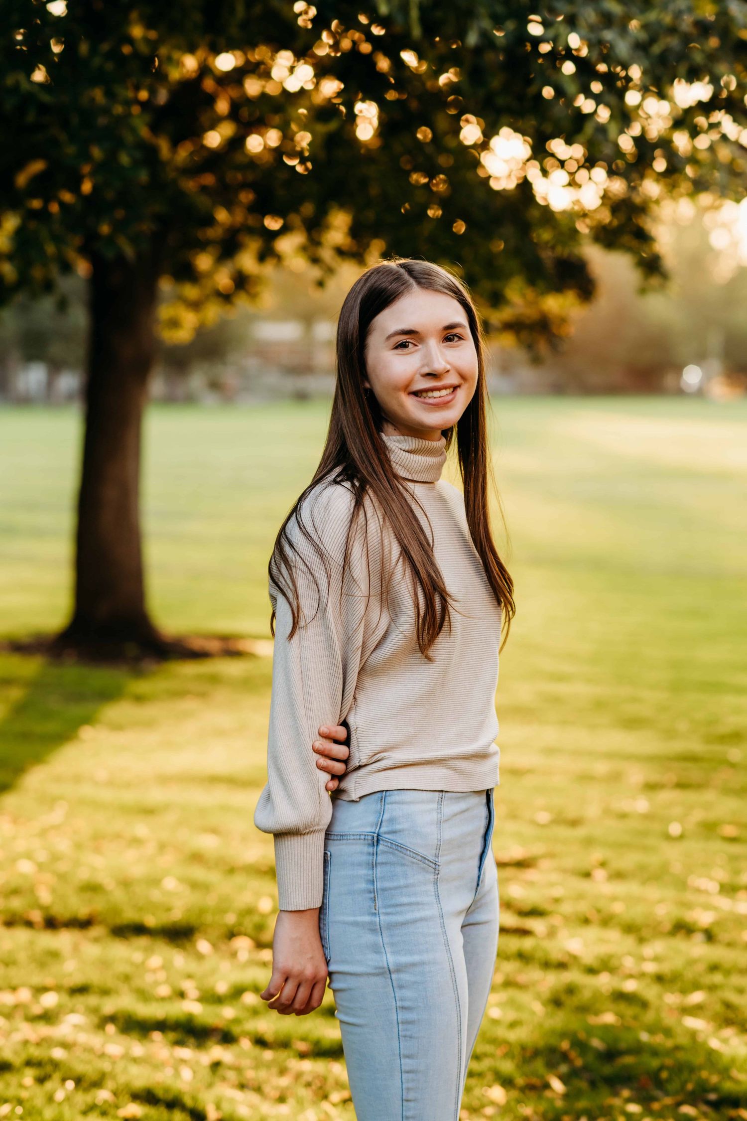 A casual portrait of a senior smiling at the camera with a grassy field and tree in the background at Whitman College in Walla Walla.