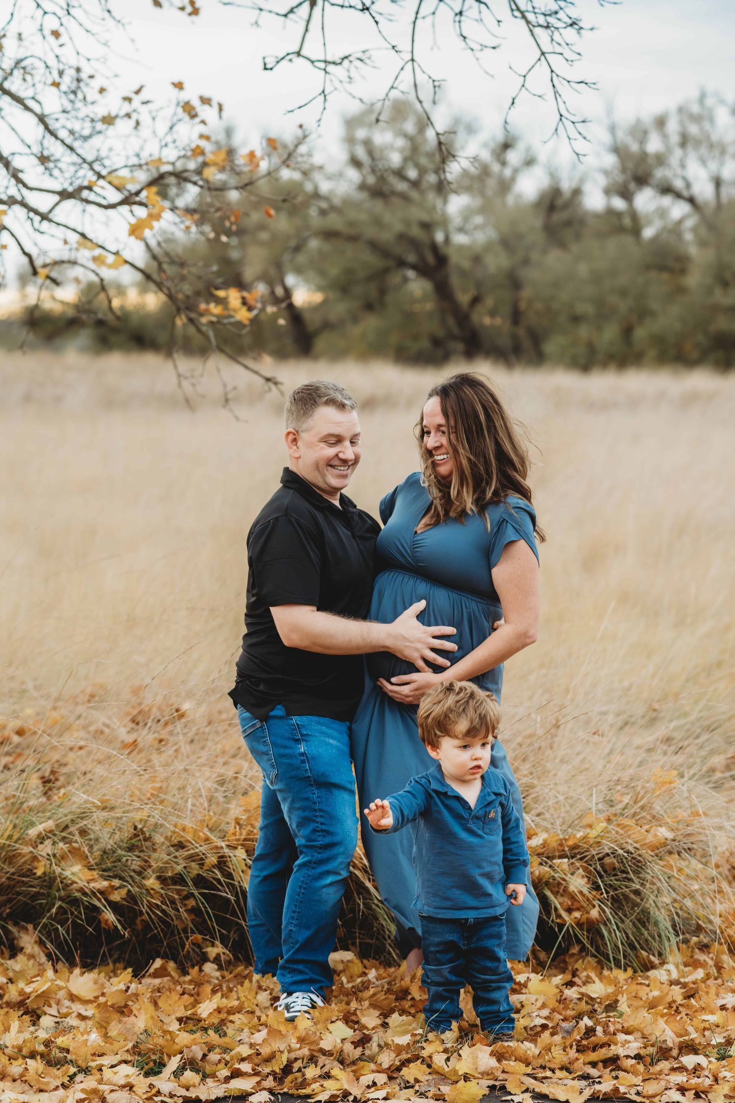 A pregnant couple embraces each other while they watch their toddler play in the leaves at Whitman Mission in Walla Walla.