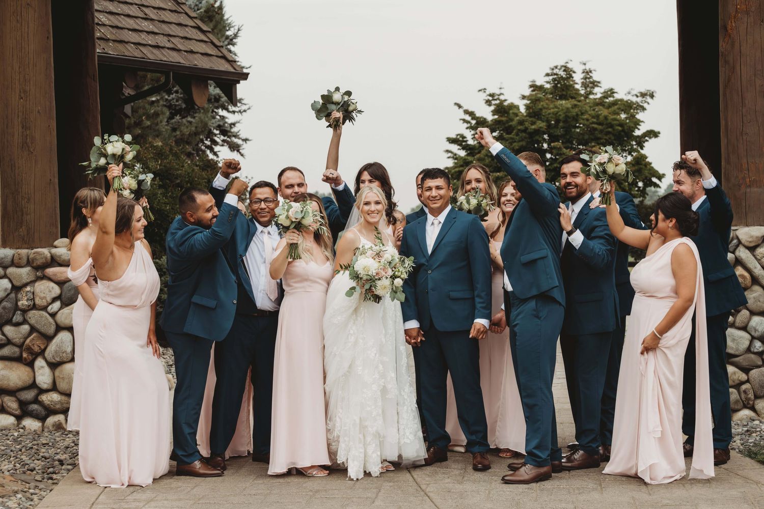 A bridal party holding up their bouquets and looking at the bride and groom as they smile for the camera.