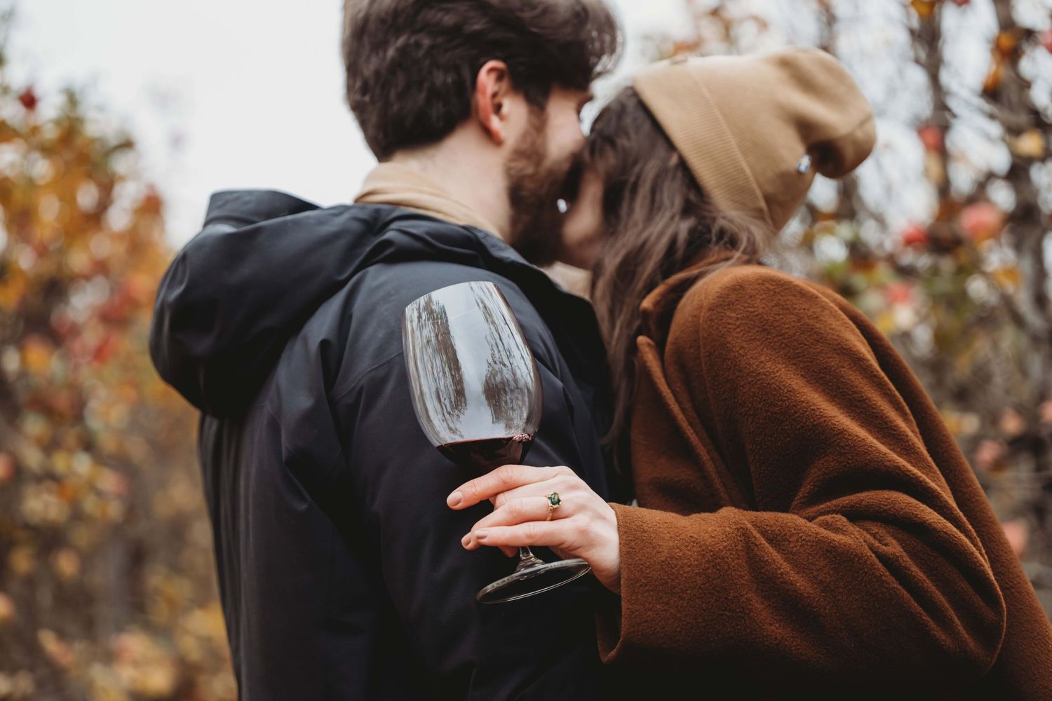 A man and woman laughing with a wine glass in an apple orchard.