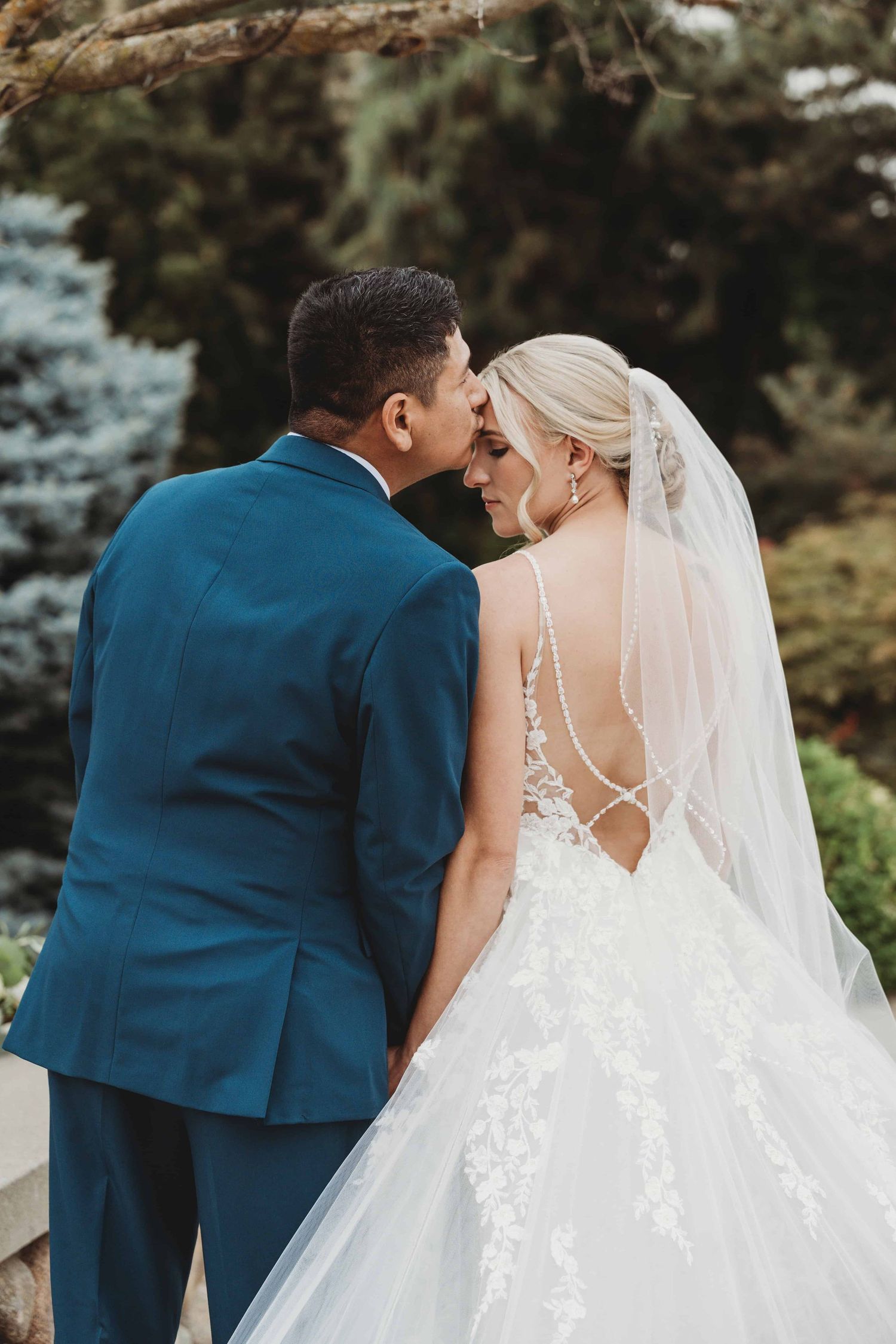 A man kissing his bride on the forehead in a classic wedding portrait.