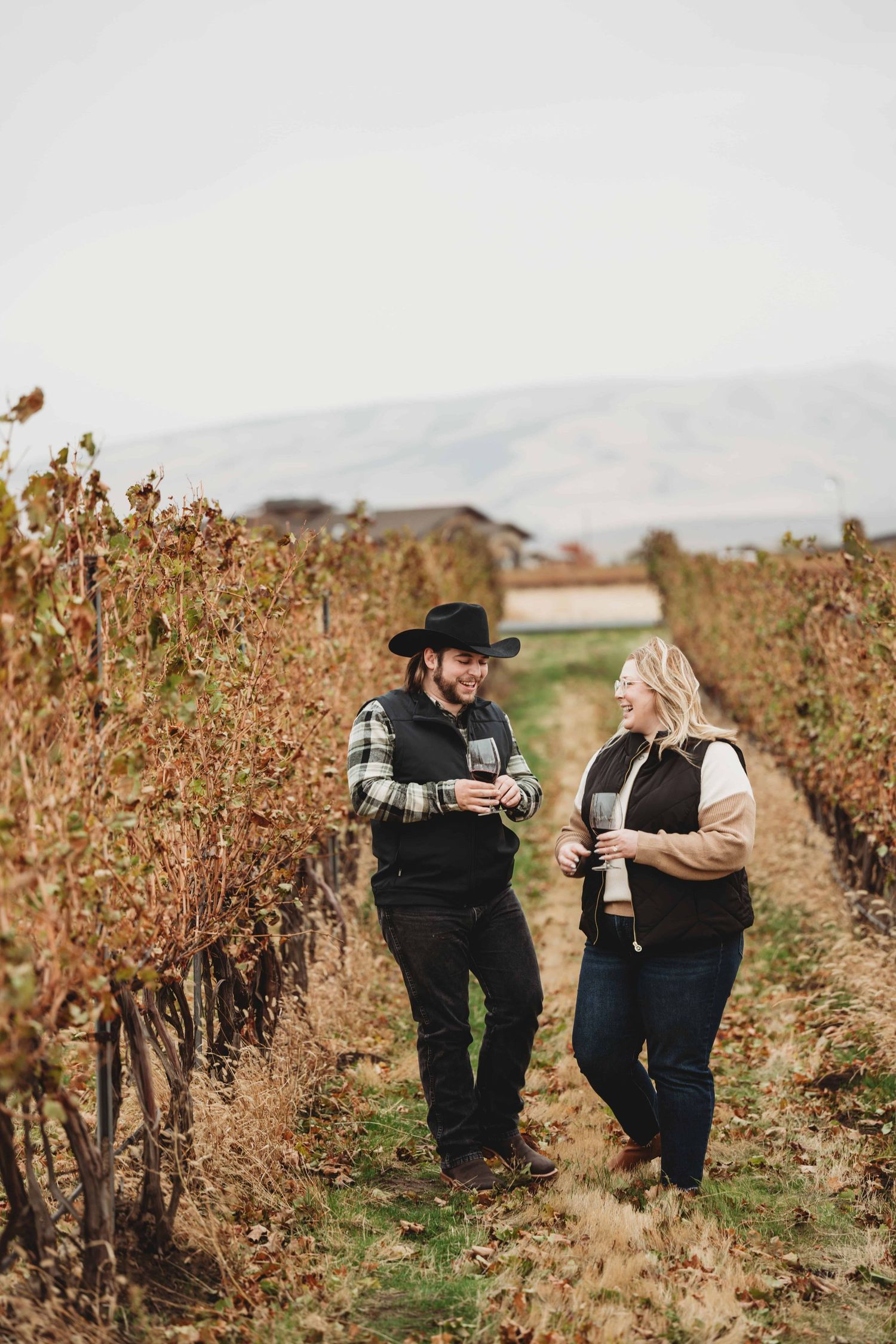 A couple holding wine glasses walks through grape vines at Pepper Bridge Winery in Walla Walla.