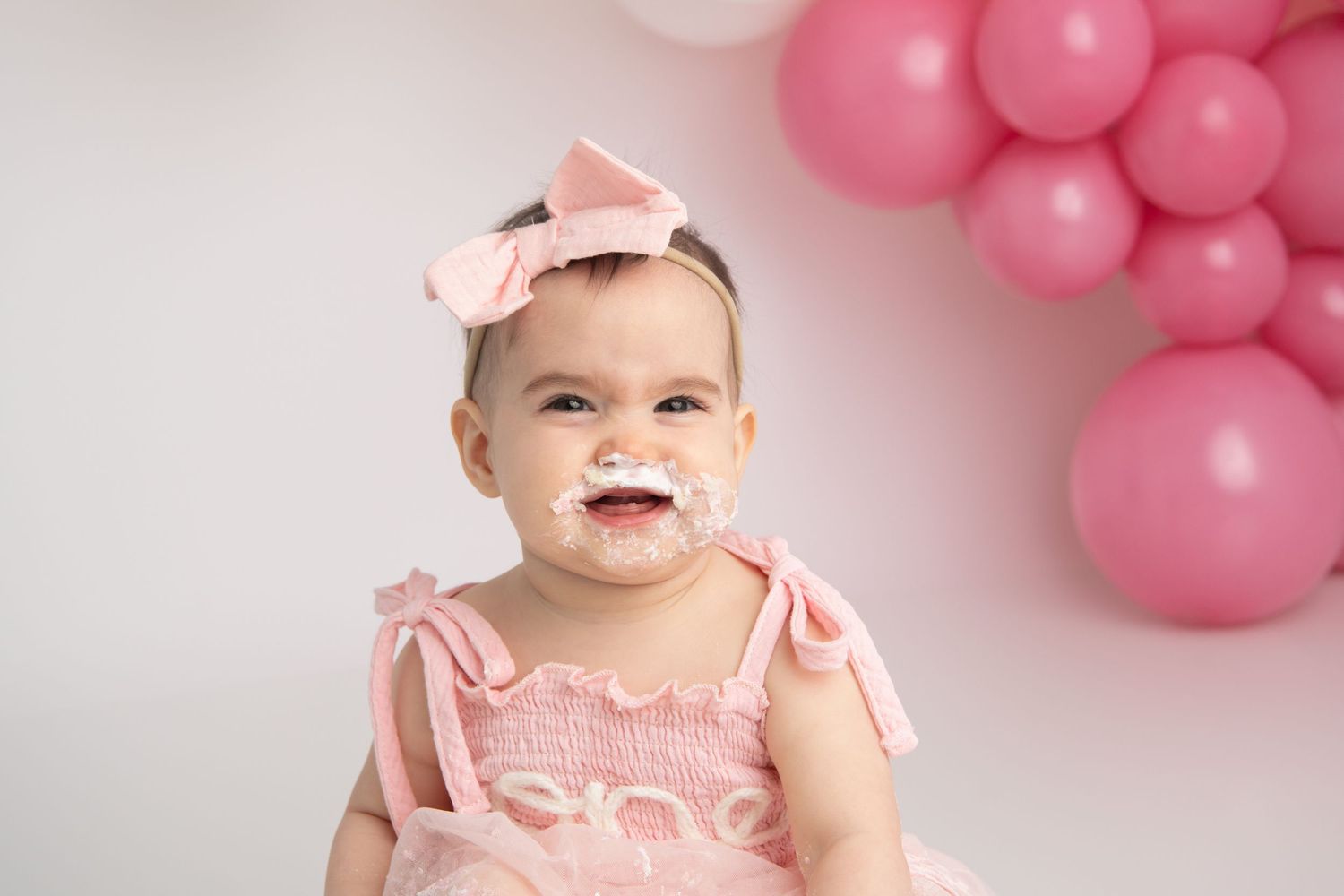 A portrait of a one year old girl with her face covered in frosting.
