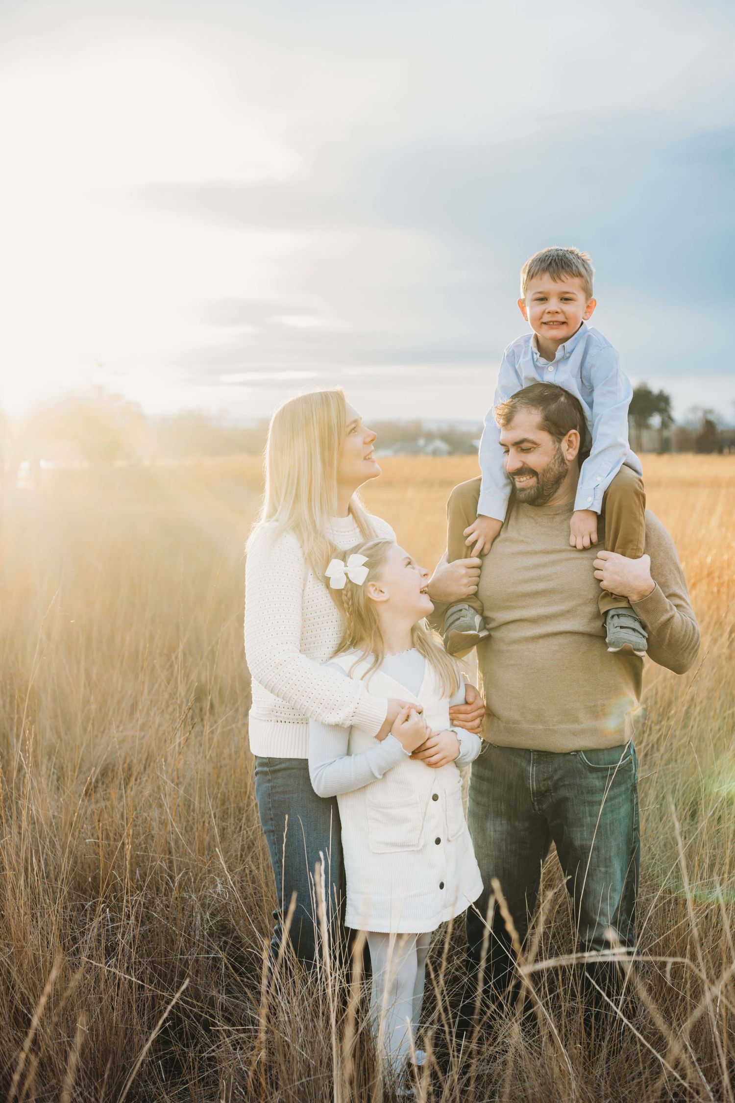 A candid portrait of a family standing in a field with a boy on his dad's shoulders during golden hour at Whitman Mission in Walla Walla.