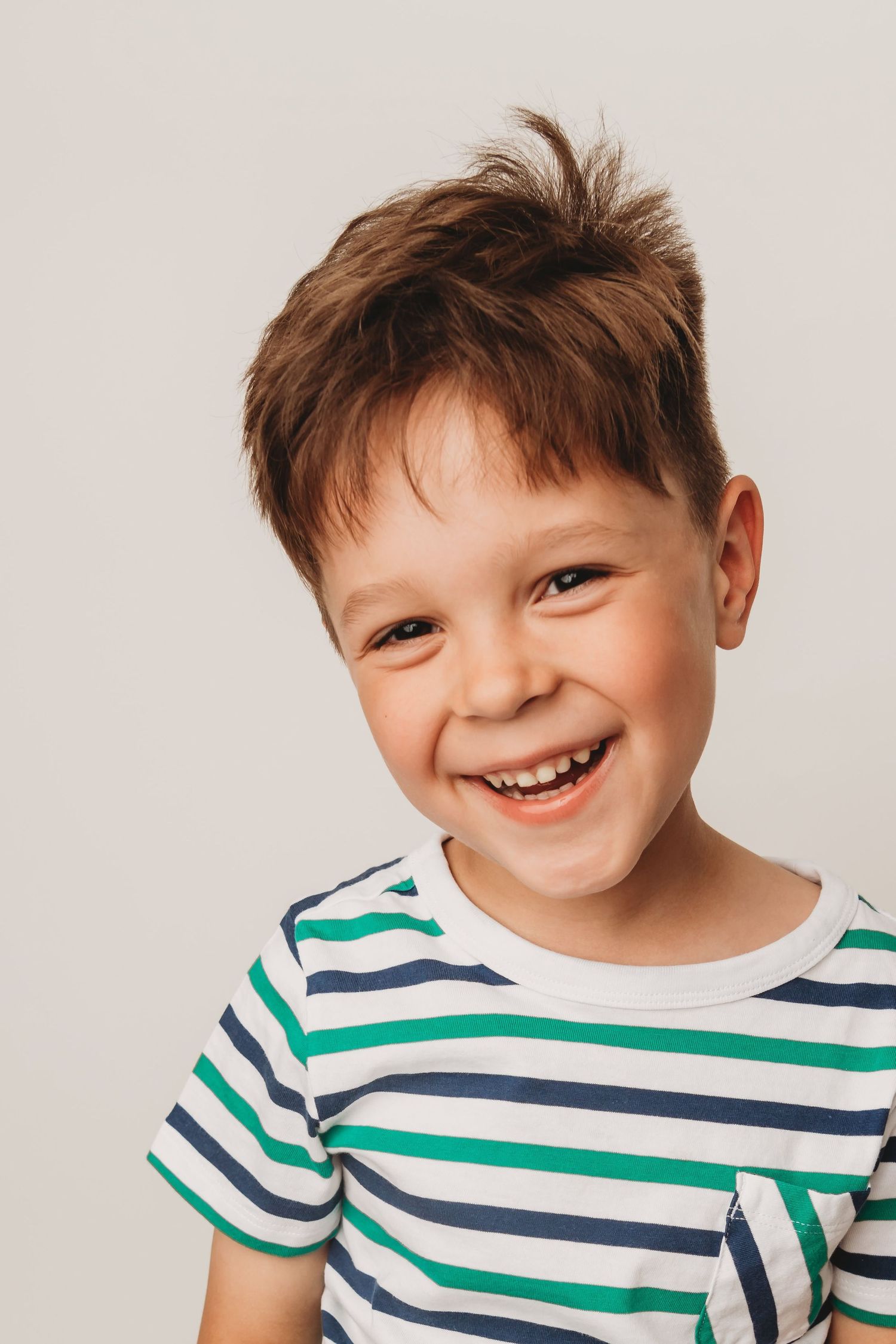 A boy wearing a white, green, and blue striped shirt and smiling.
