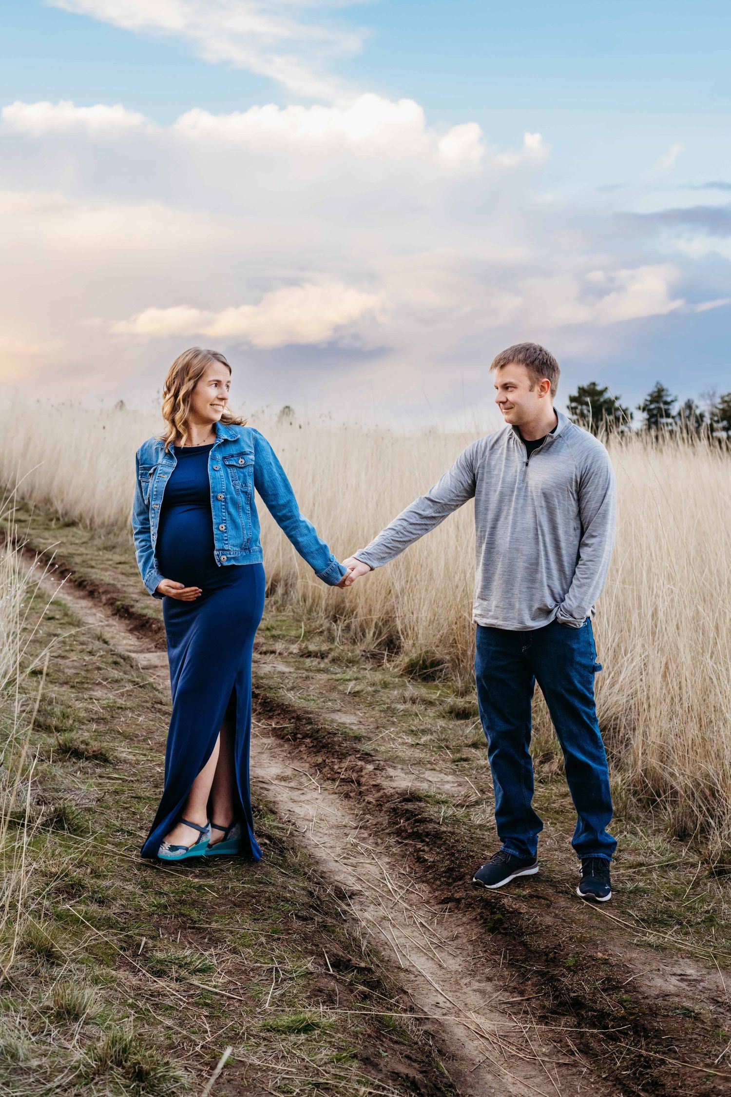 Pregnant couple holding hands while walking along a grassy path at golden hour, photographed during an outdoor maternity session in Walla Wa