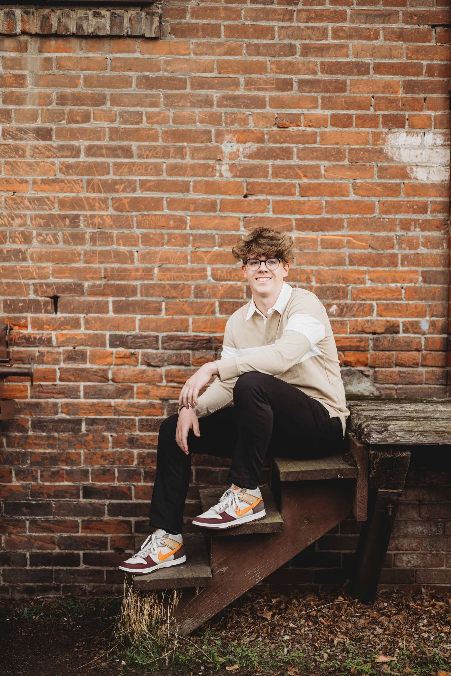A senior portrait of a young man sitting on some wooden steps with a brick building as the background, taken by a Walla Walla photographer.