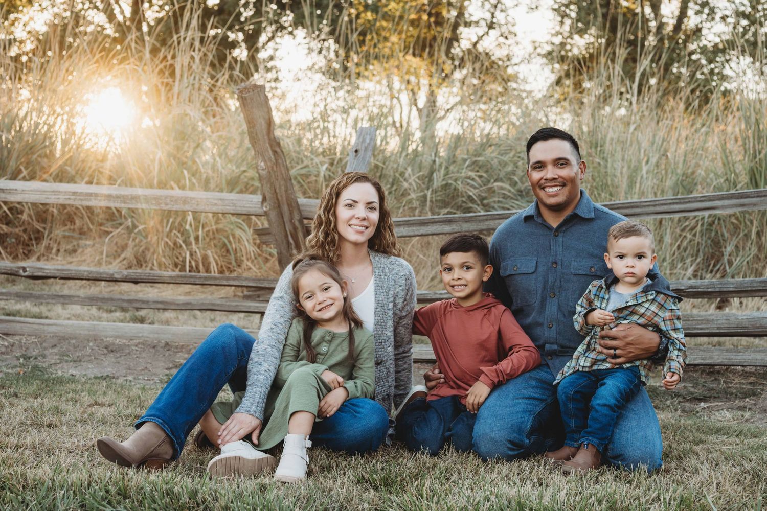A family sitting on the ground in front of an old wooden fence.