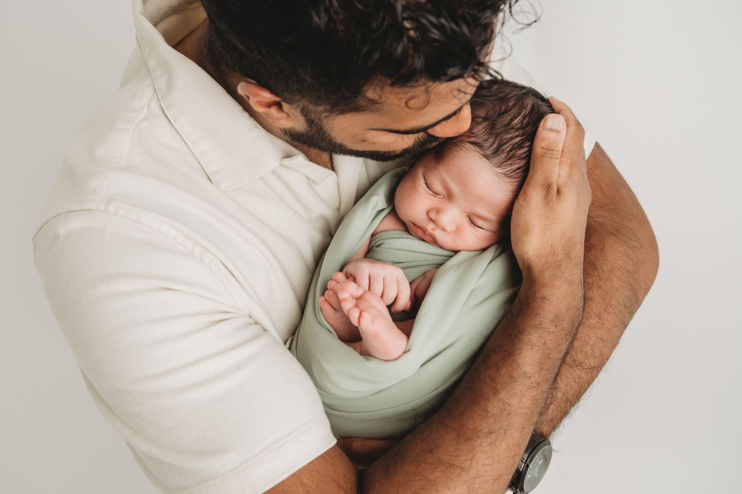 A father snuggling his baby boy wrapped in sage green, taken by a Pasco, Washington newborn photographer.