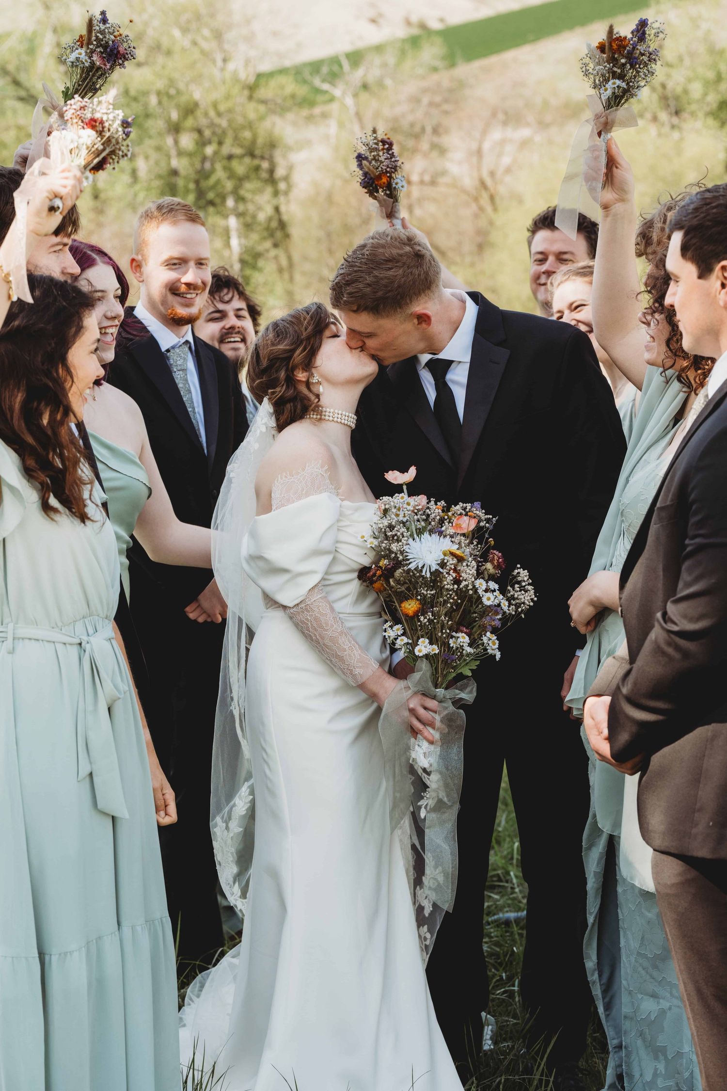 A couple kissing with their bridal party surrounding them and cheering them on.