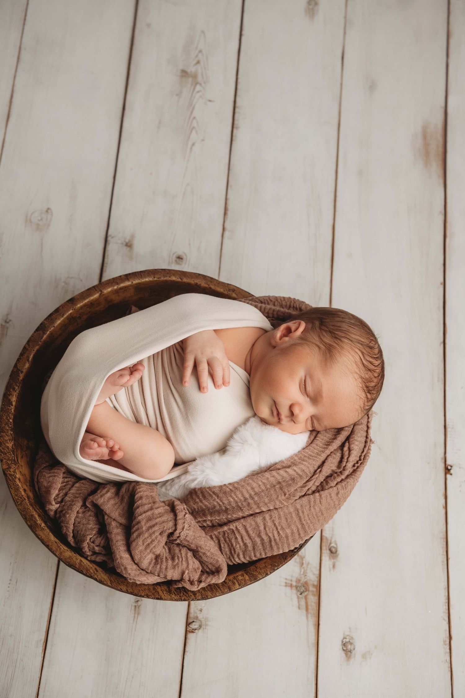 A newborn wrapped in cream sleeping in a brown wooden bowl at a newborn photography studio in Walla Walla.