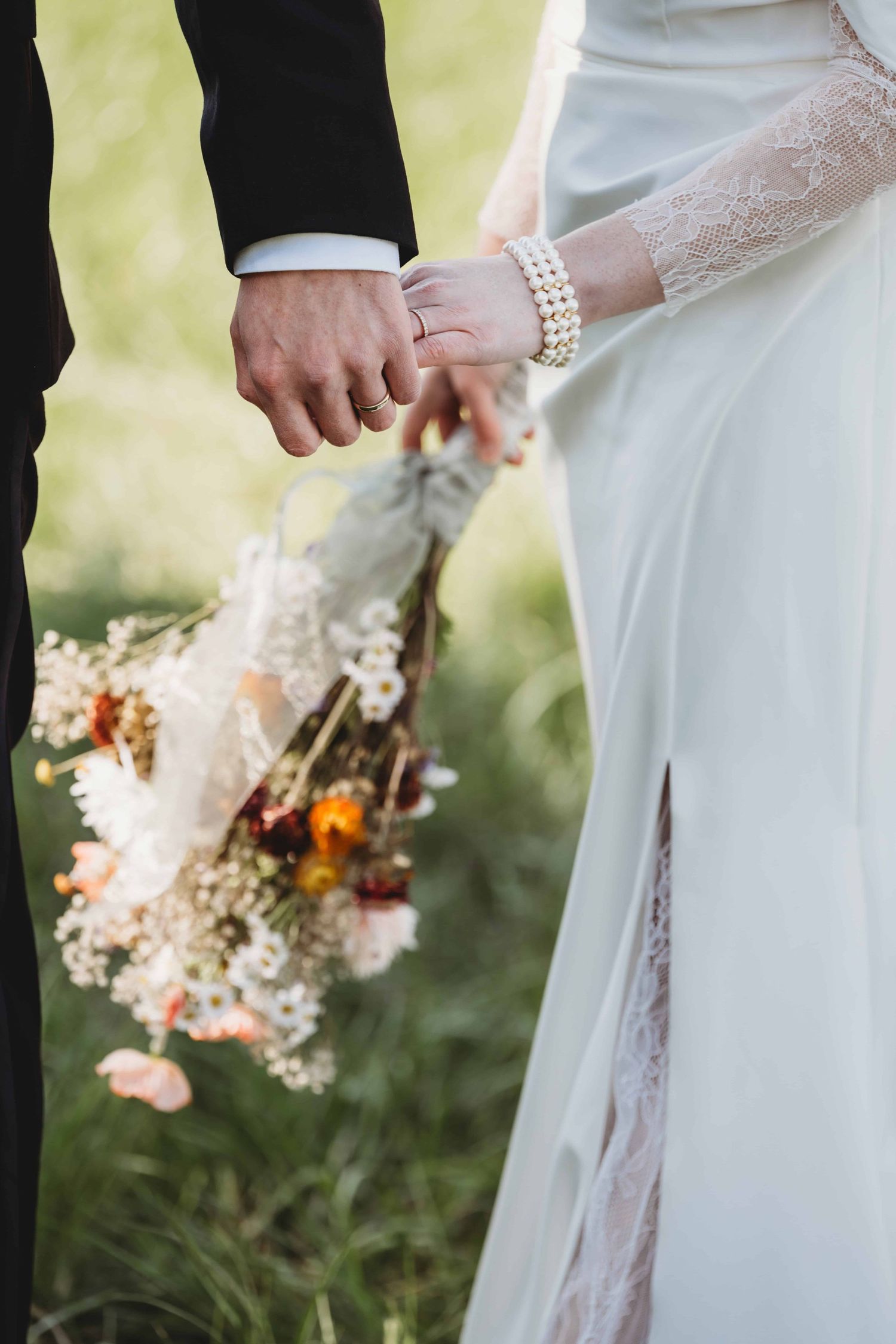 A close up of a bride and groom holding hands and the wedding bouquet made of wildflowers