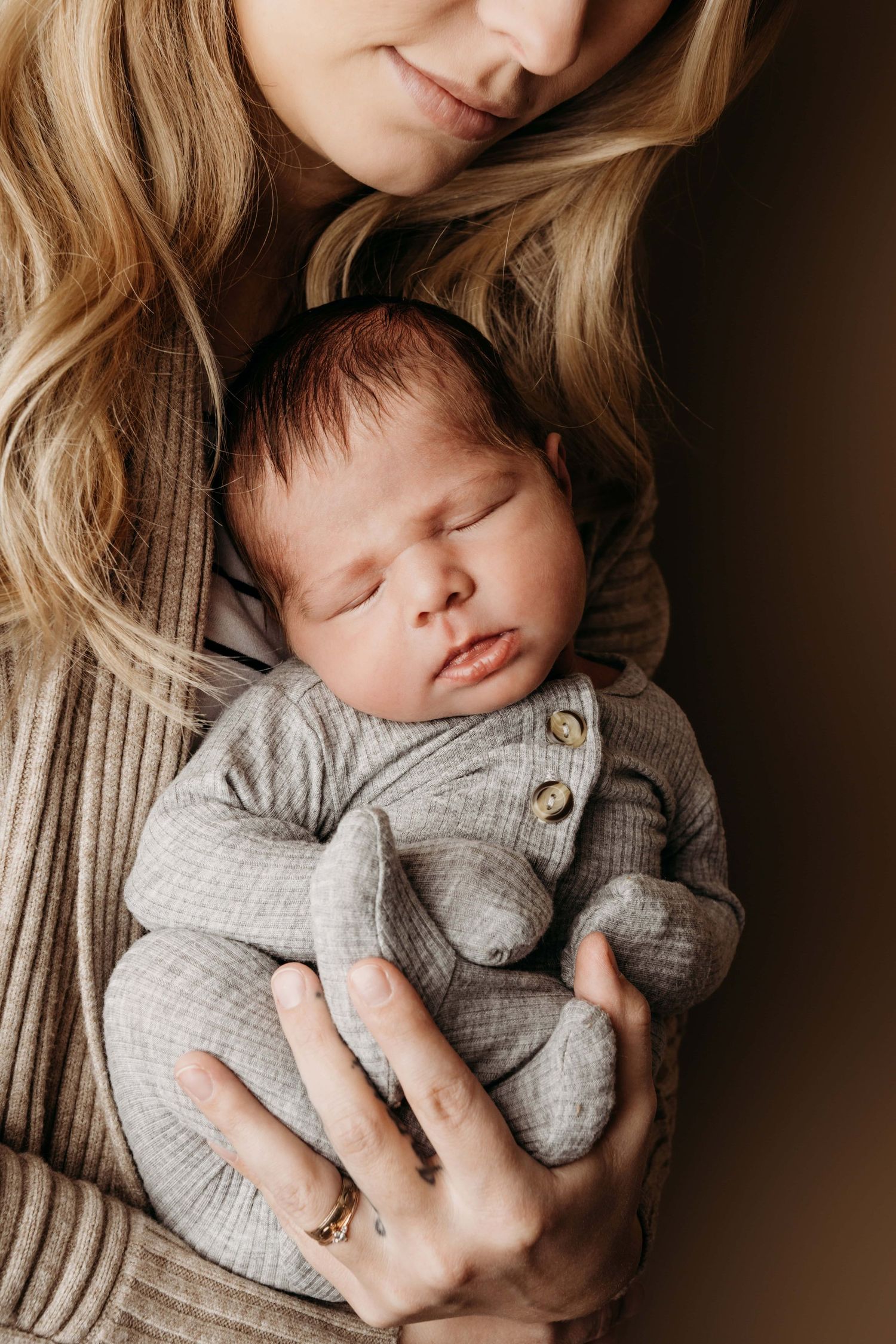 A newborn wearing a gray outfit sleeping in their mother's arms.