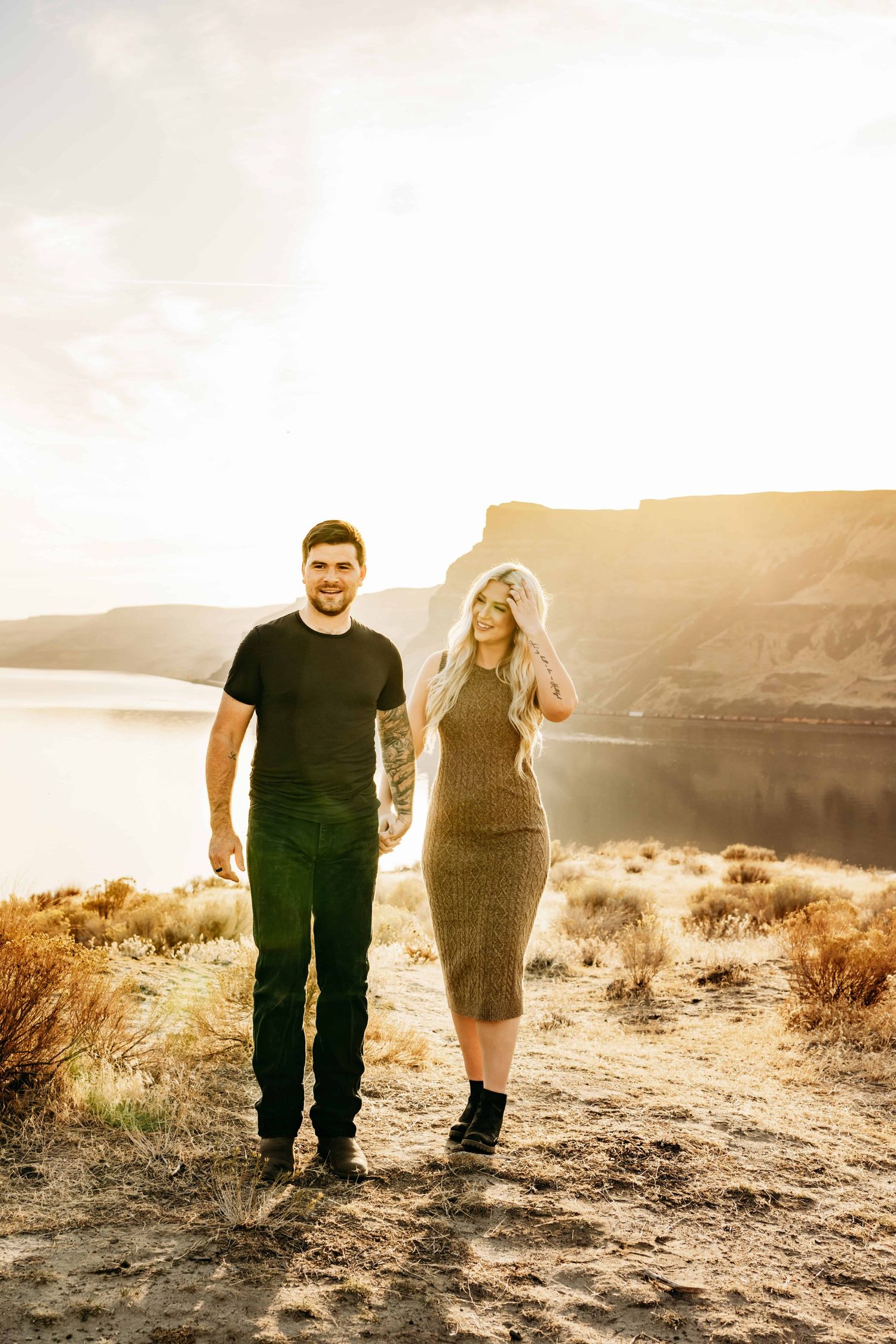 Dramatic golden hour portrait of a couple walking above a river holding hands.