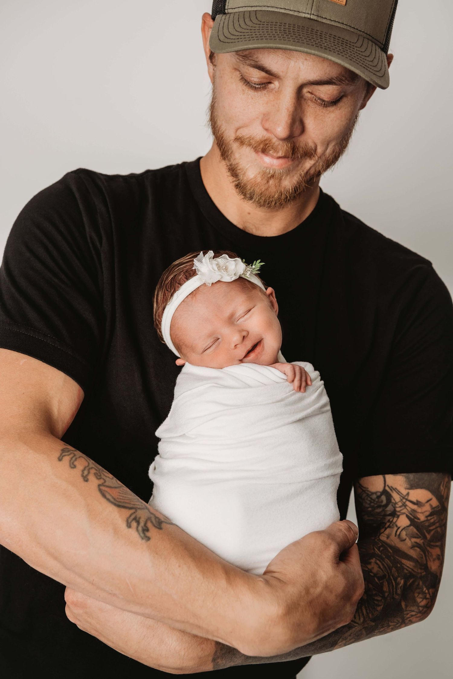 A new dad holding his newborn daughter wrapped in a white blanket and looking down at her.