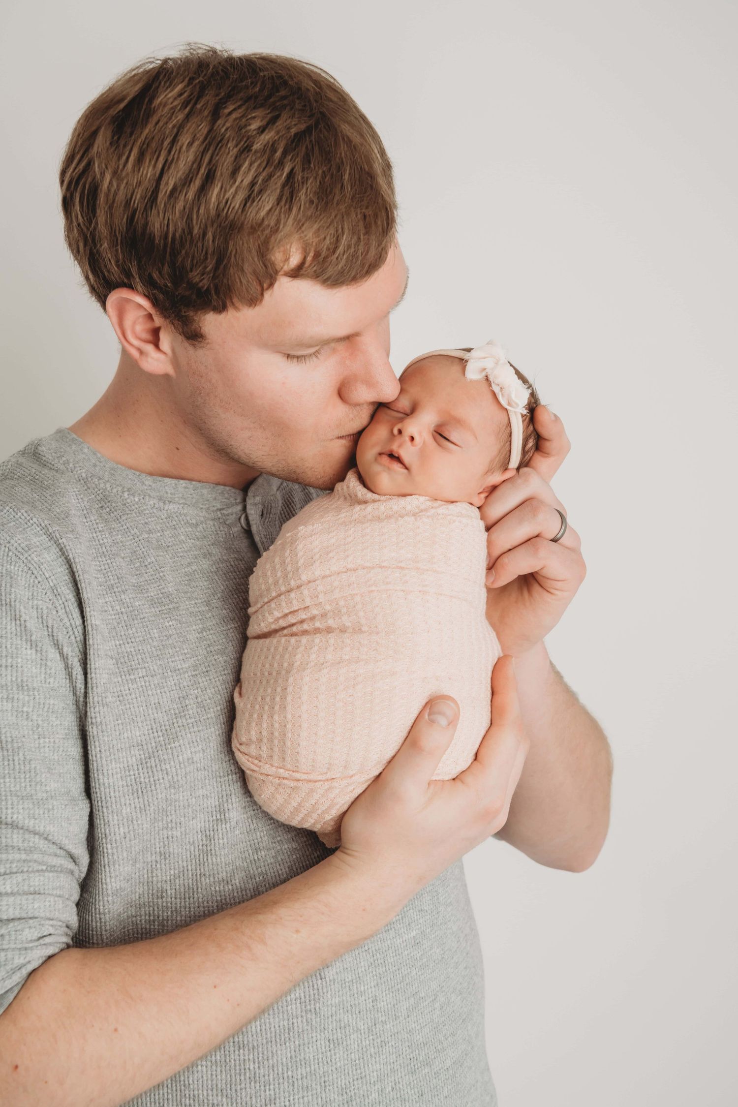 A dad kissing his newborn's head on a neutral backdrop.