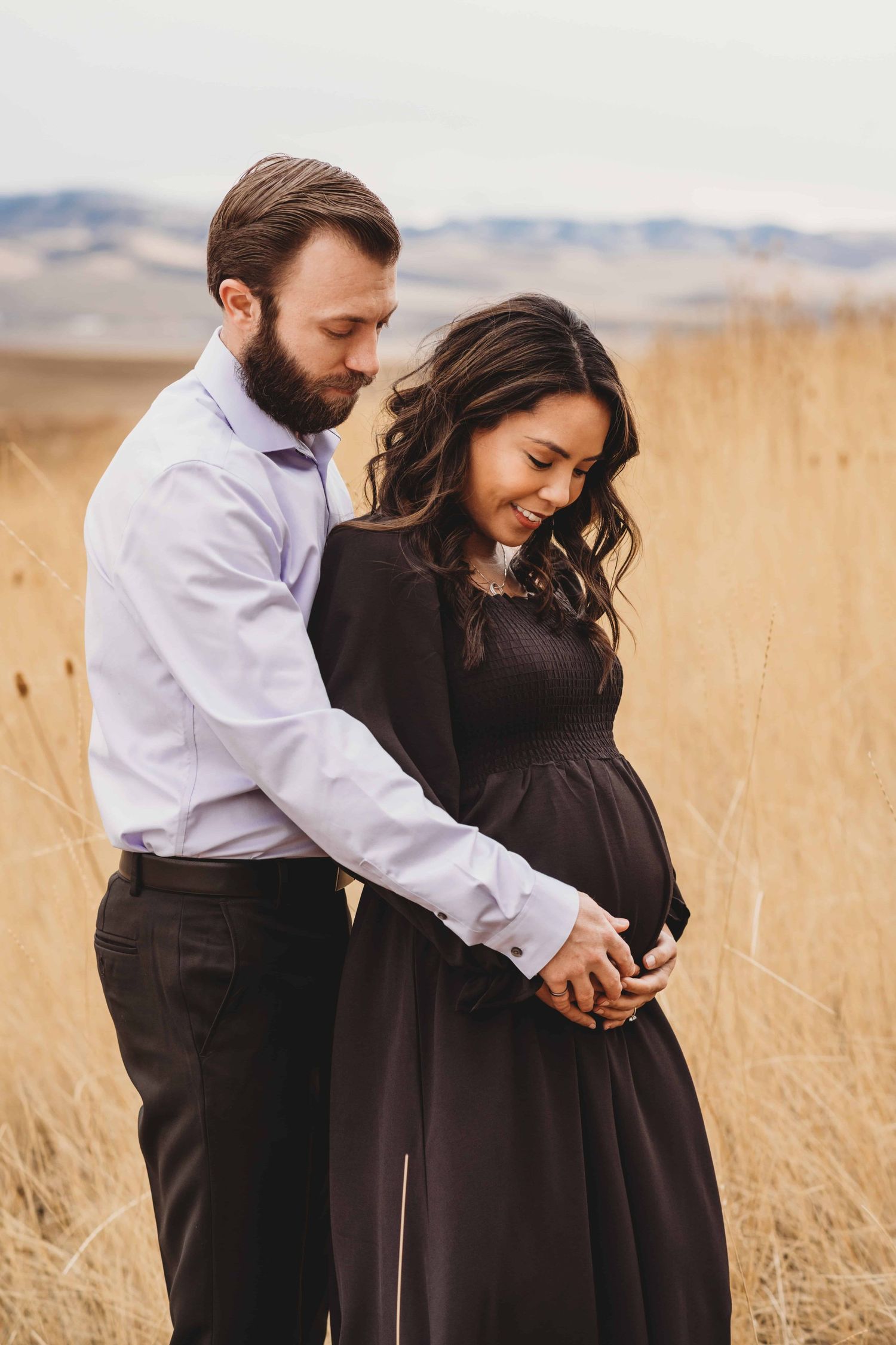 An expecting couple looks down at the baby bump smiling with anticipation.