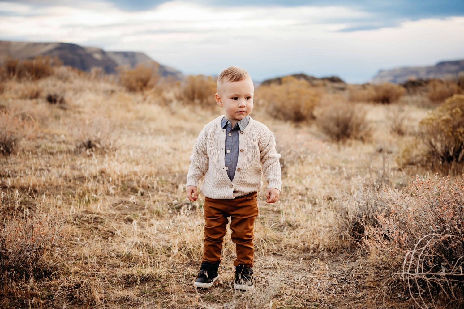 A portrait of a child standing in a field with a serious expression.