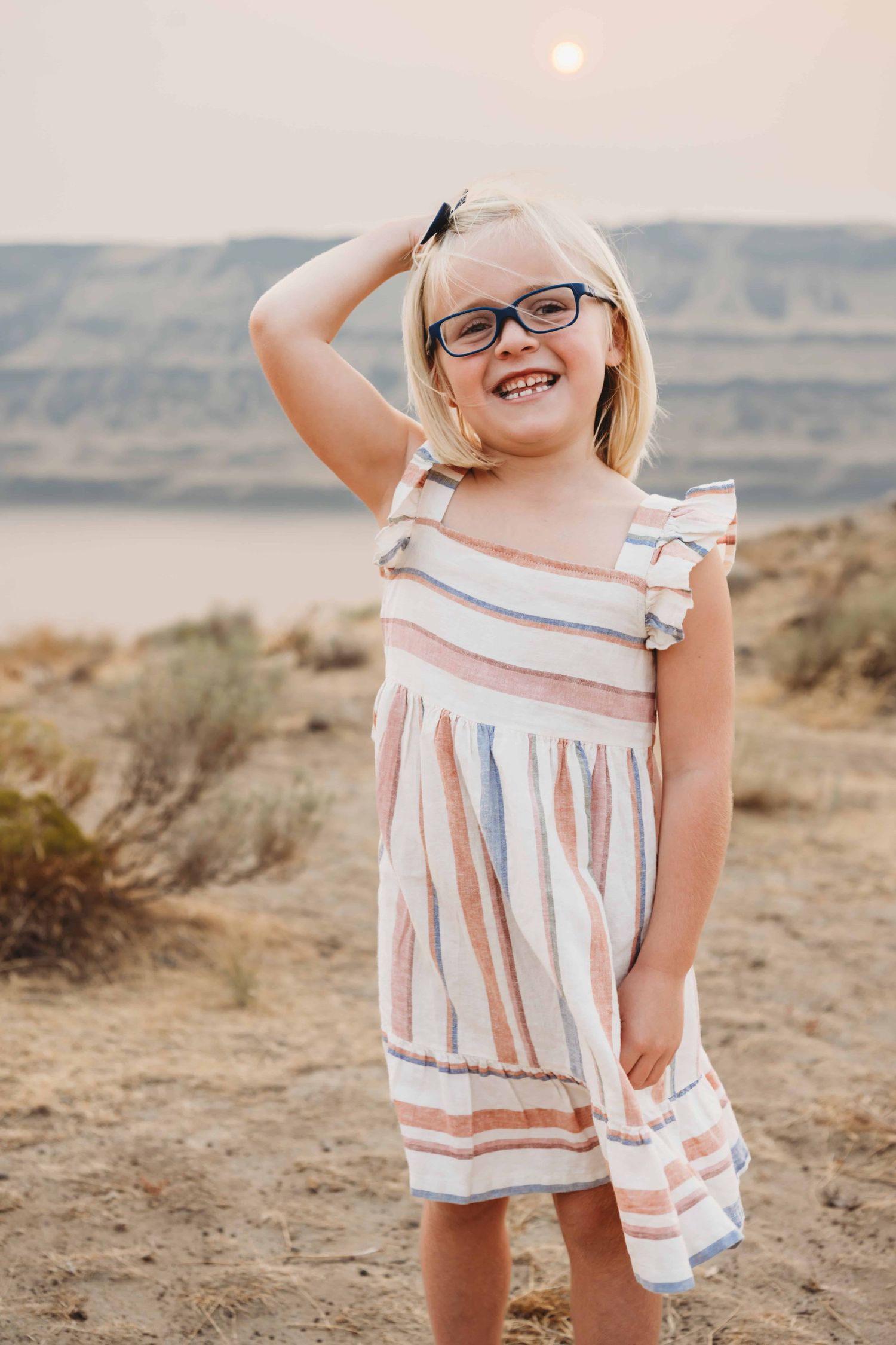 A girl standing with mountains and a river in the background.