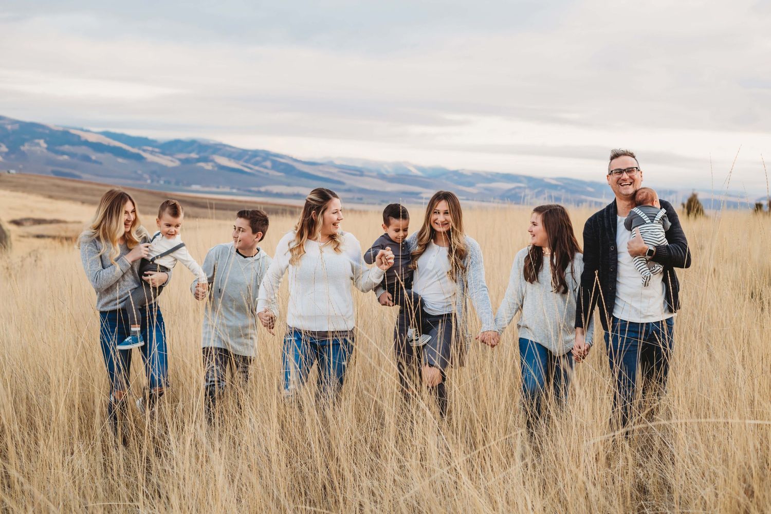 Family of nine walking in a field with the blue mountains in the background.