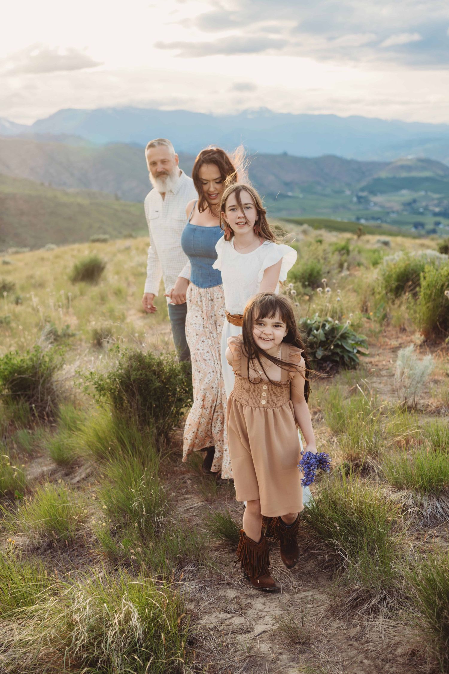 A family walking in a green field during sunset with mountains in the background.