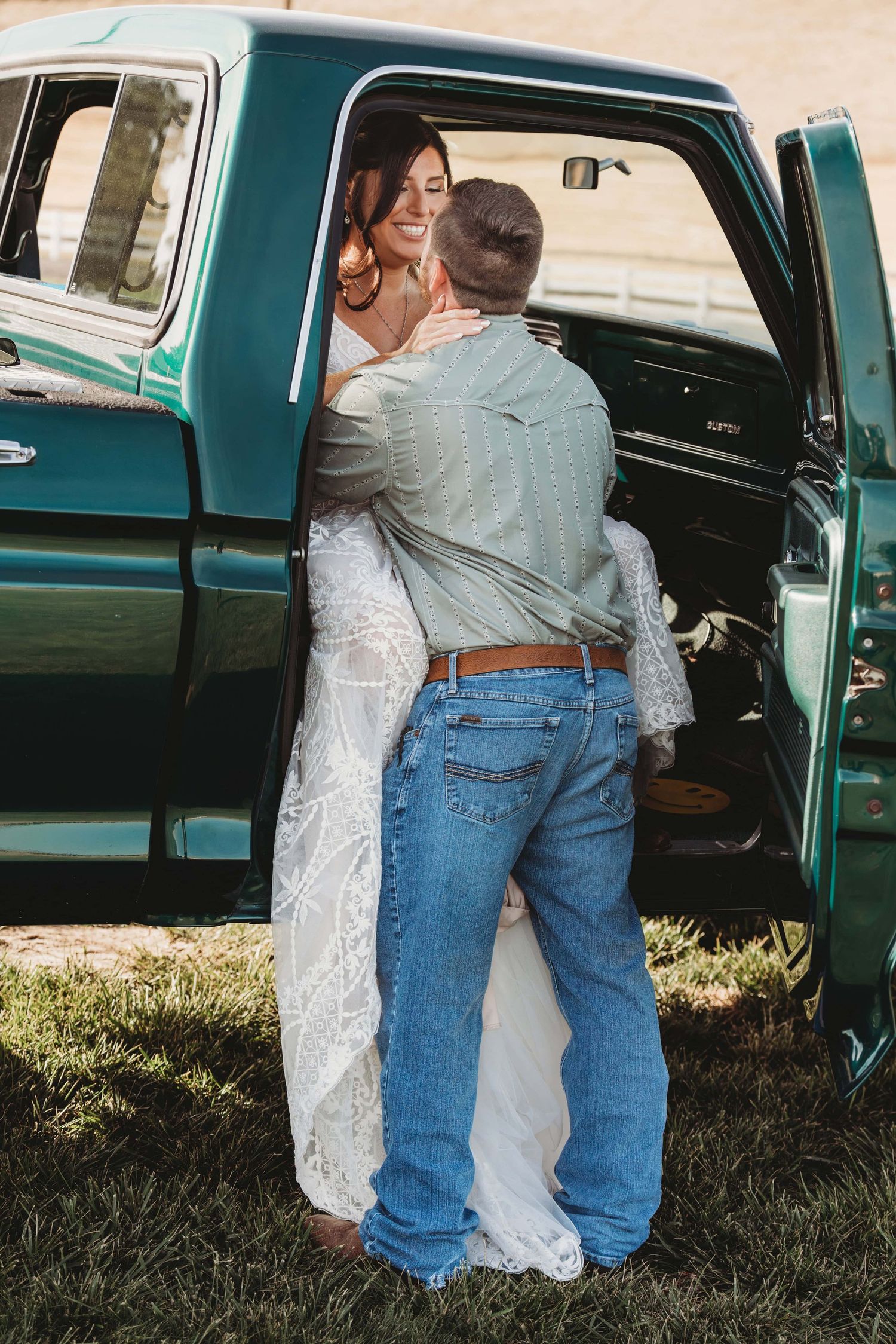 A bride sitting in an old green truck while her groom leans in and looks at her