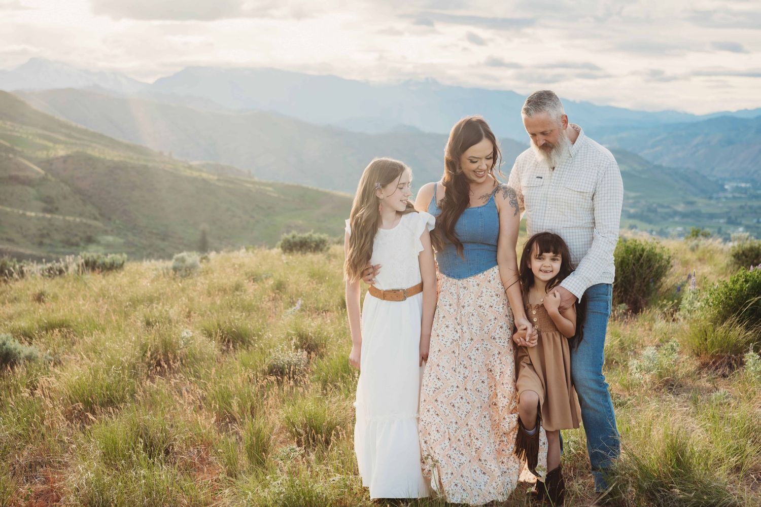 A little girl looking at the camera while her family looks down at her, during a golden hour session in Leavenworth Washington.