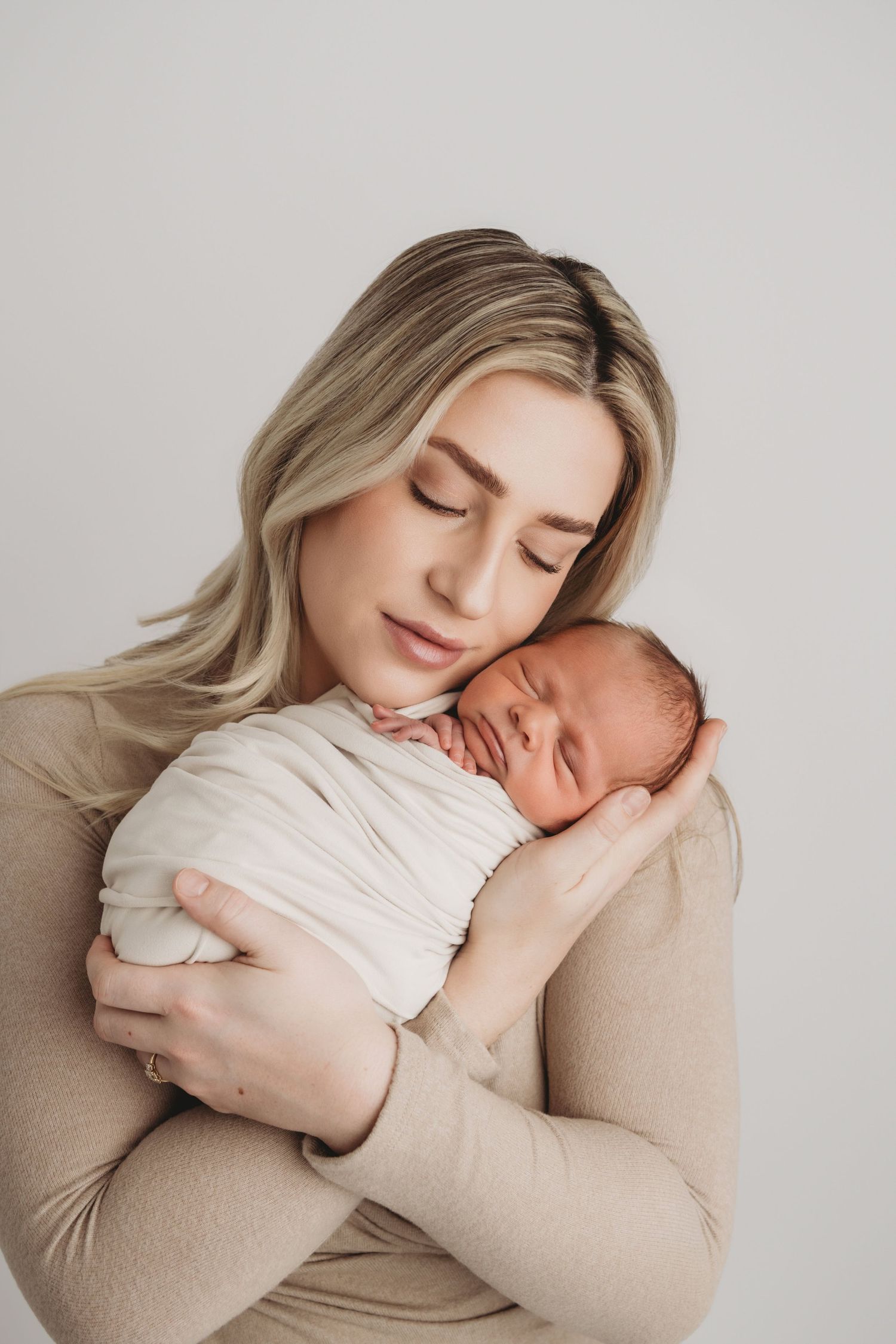 A mother snuggling her newborn baby boy as he sleeps peacefully, taken by a Tri-Cities newborn photographer.