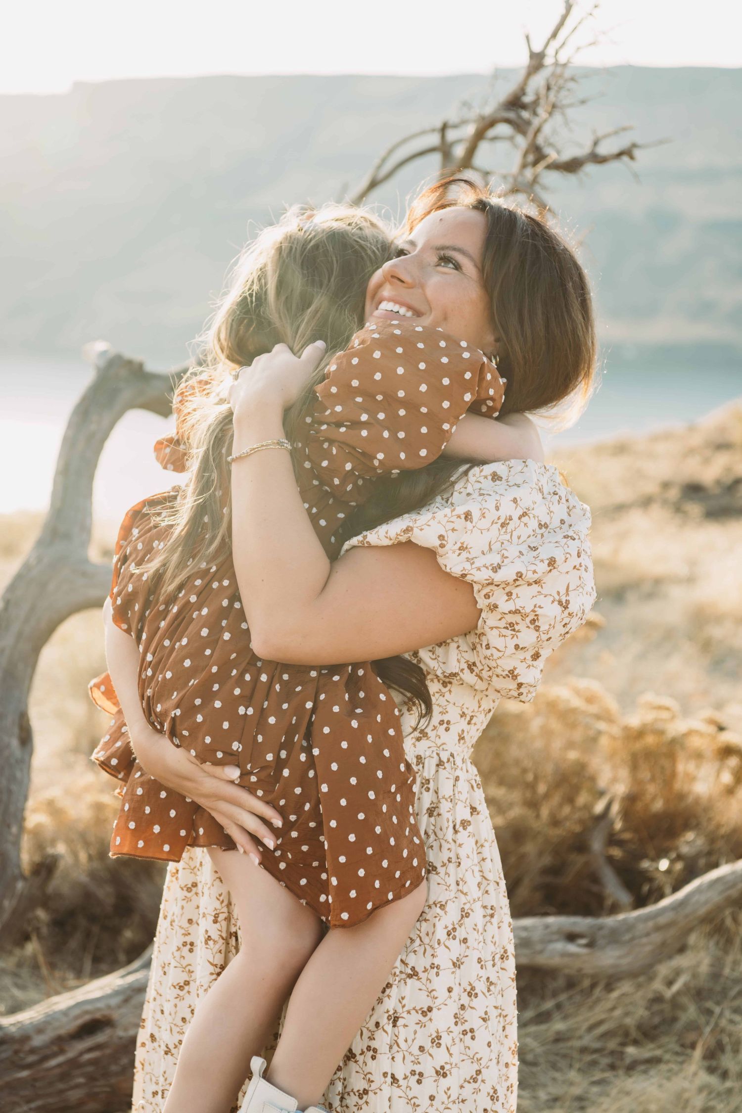 A mother embracing her daughter in front of a desert landscape during golden hour.