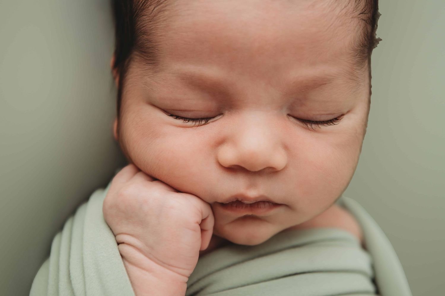 A close up portrait of a newborn baby boy wrapped in green.