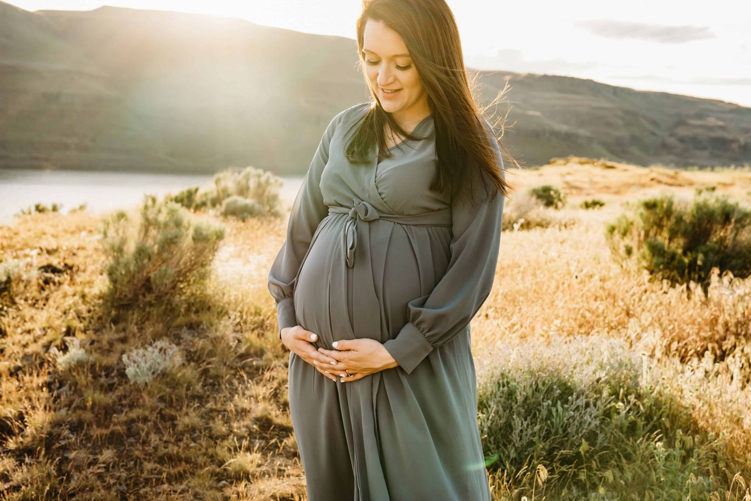 An expectant mother looking at her belly with a soft smile during golden hour.