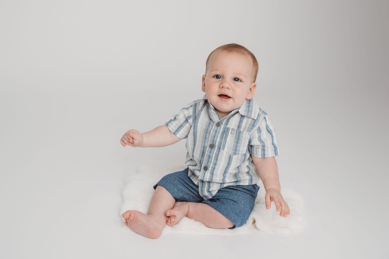 A Walla Walla photographer captures a baby sitting on a white rabbit fur mat and smiling softly.