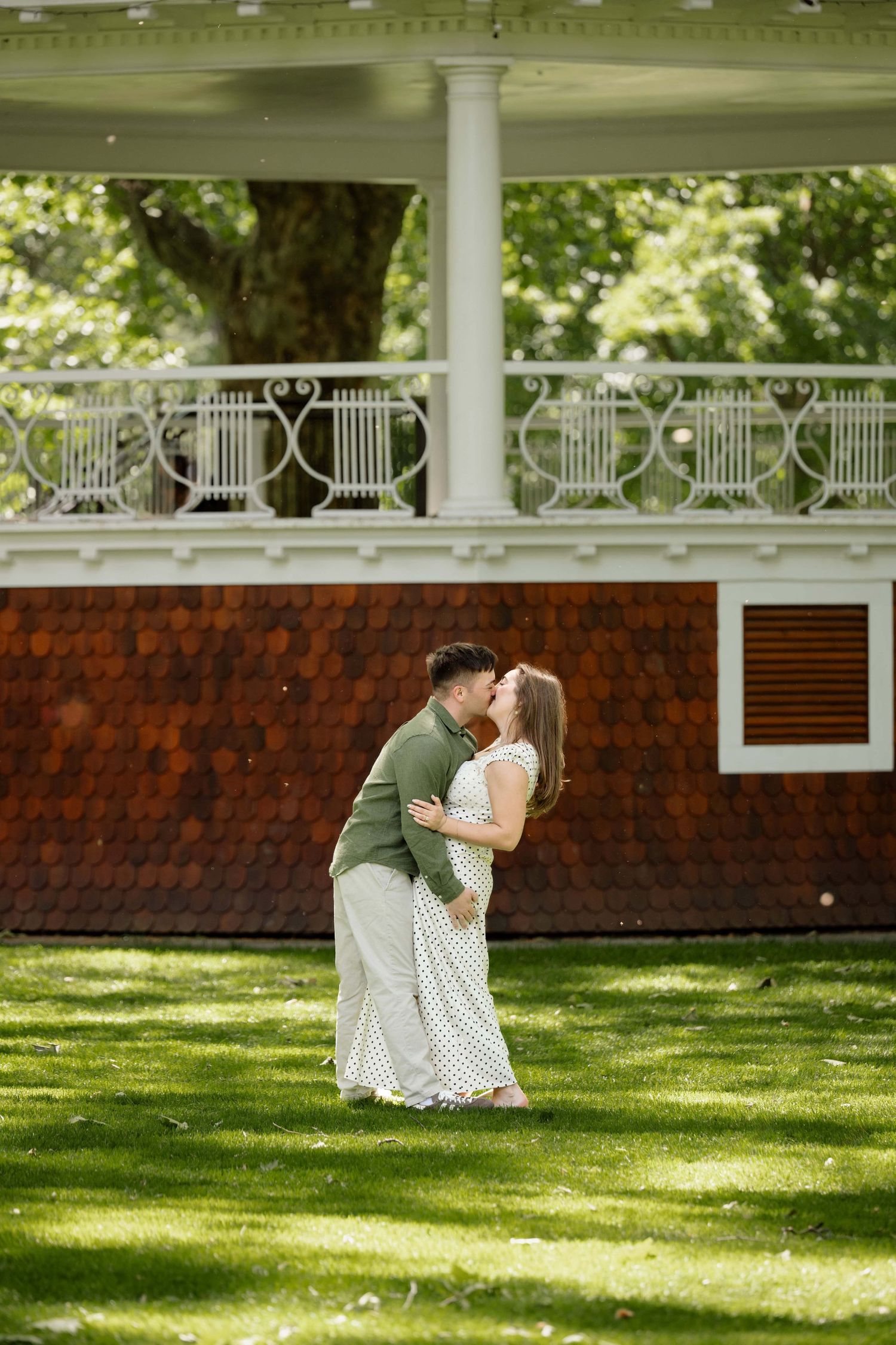 A man and woman kissing with a gazebo behind them in a lush green park in Walla Walla.