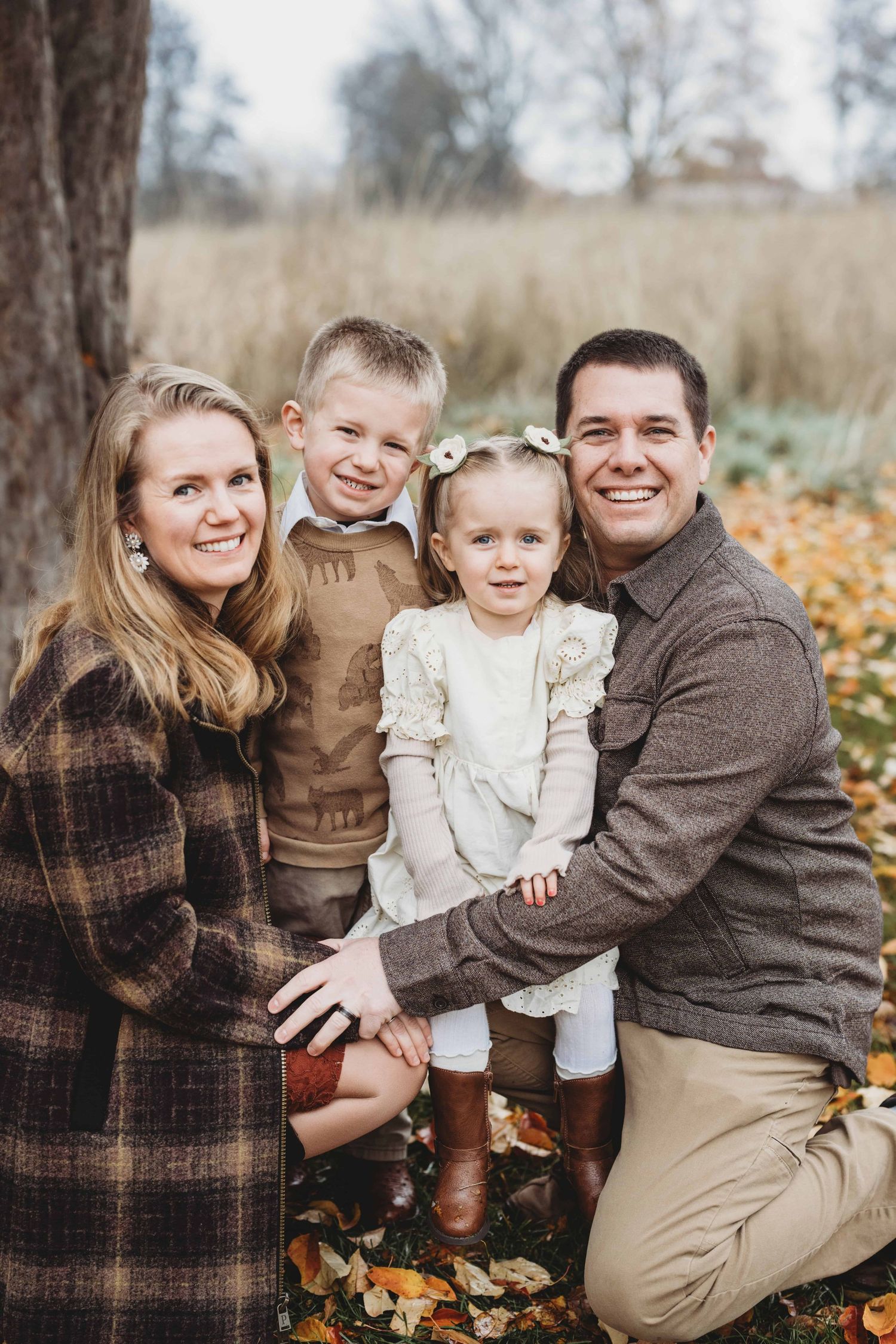 A family of four sitting among fall leaves on the ground.