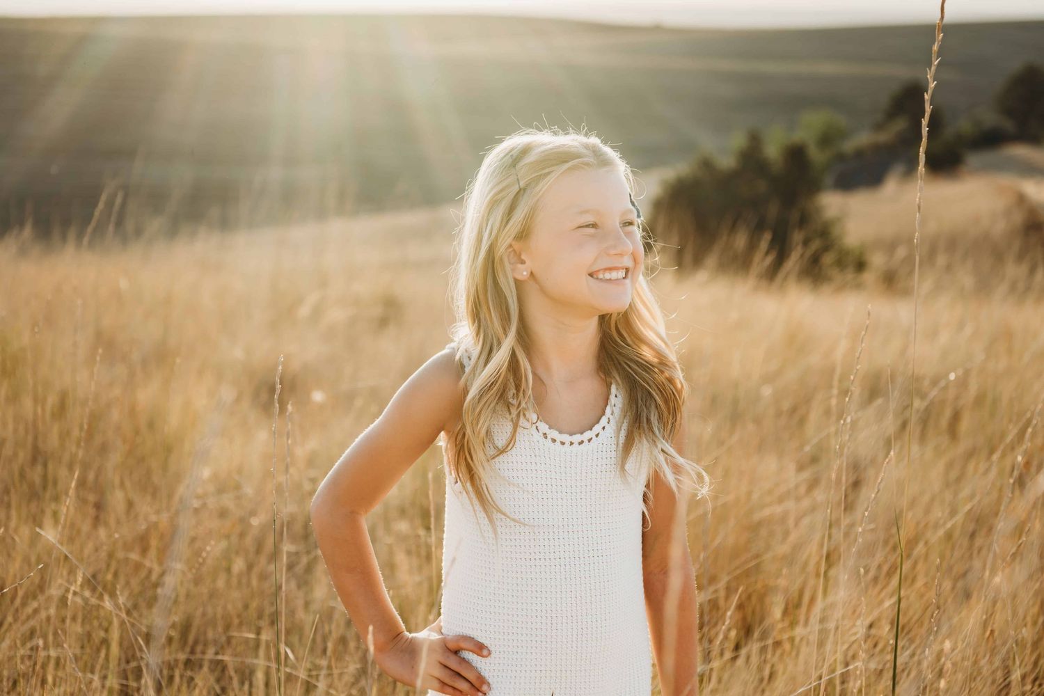 A portrait of a girl standing in a field with golden light behind her.