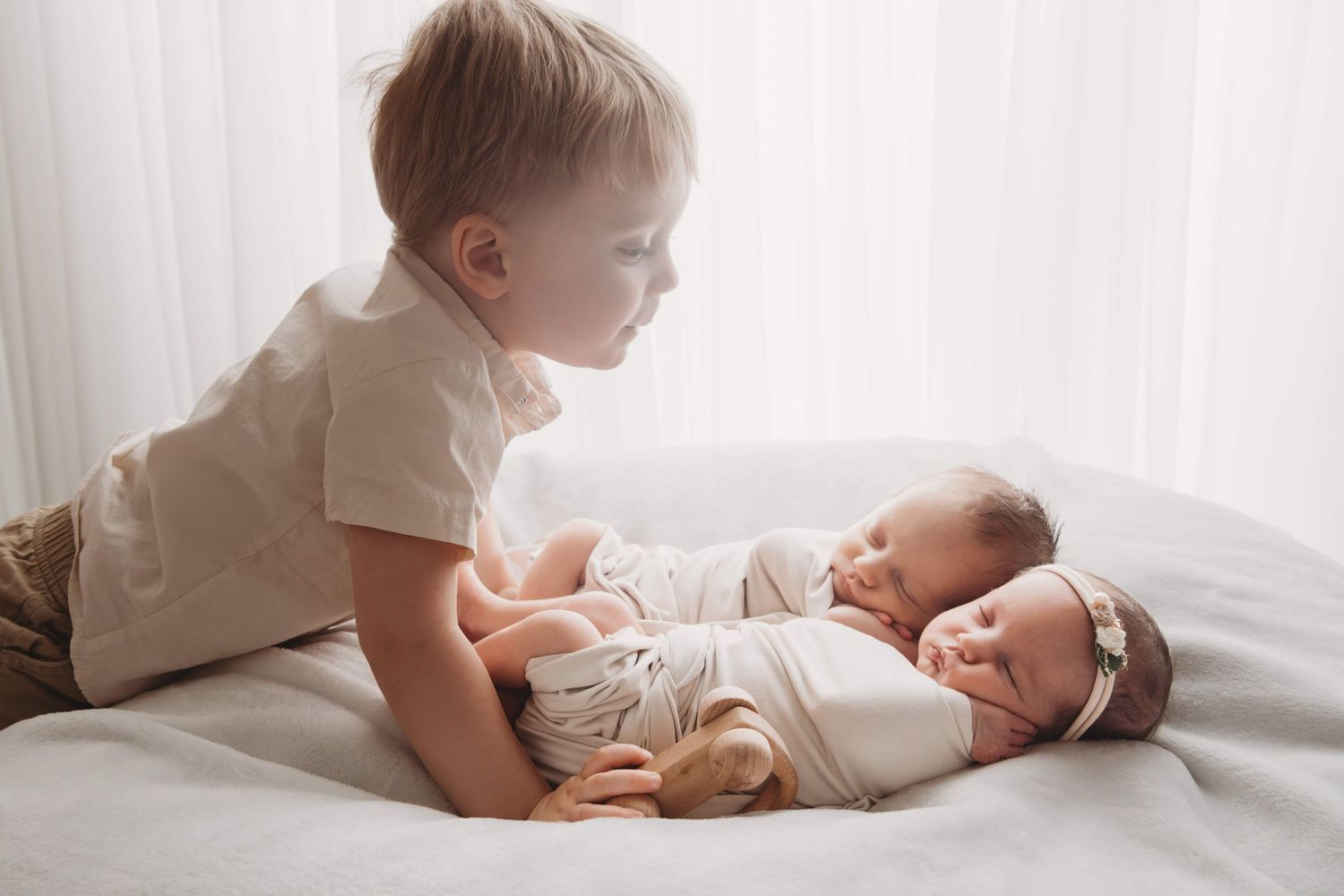 A Walla Walla photographer captures a toddler boy looking at his twin newborn siblings in a backlit studio portrait.