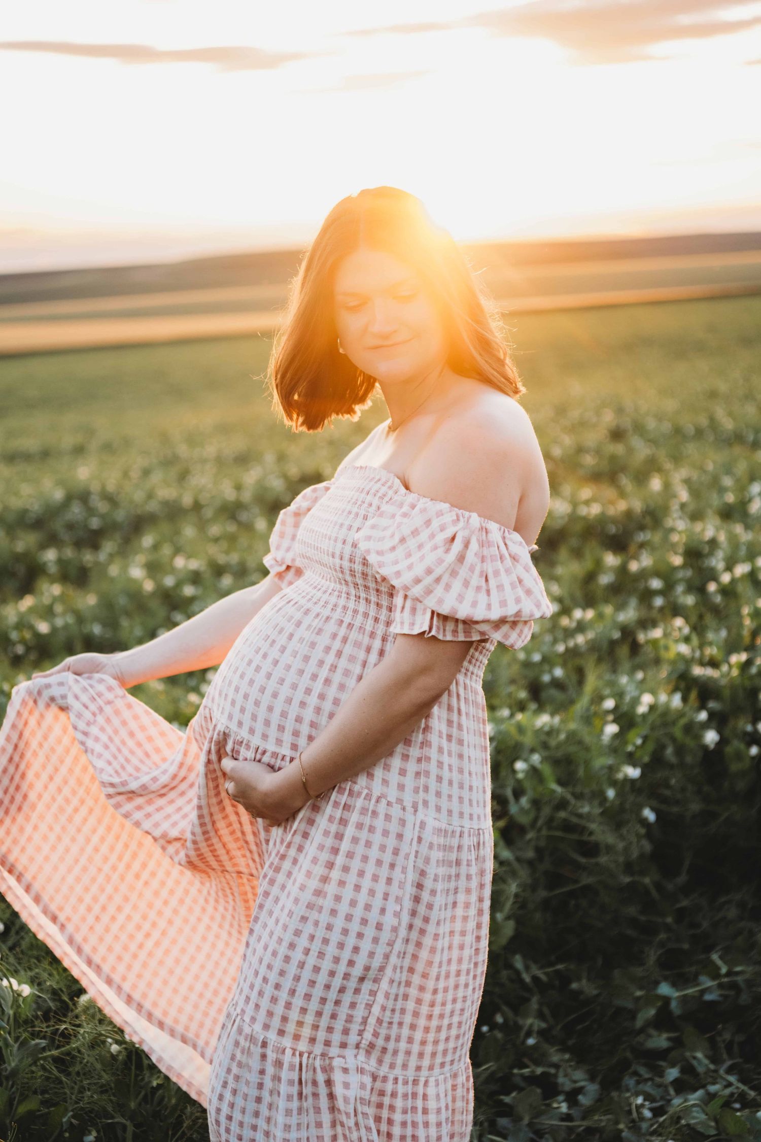 A pregnant mother fans out her dress and holds her belly while standing in a pea field with golden sunlight in Walla Walla.