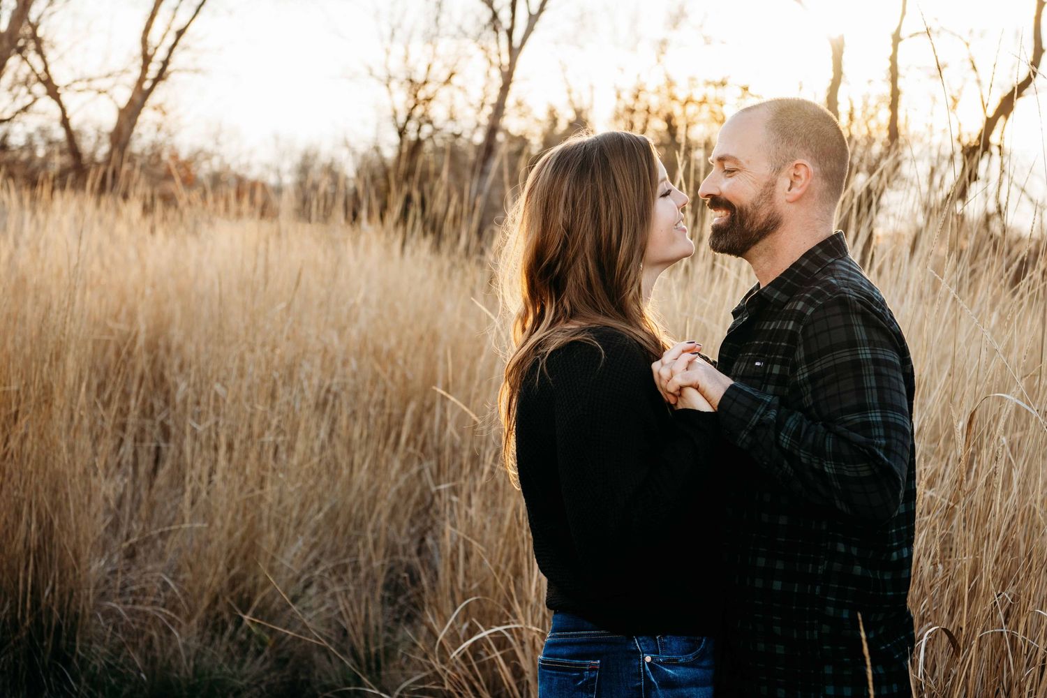 A couple wearing black holding hands and smiling at each other.