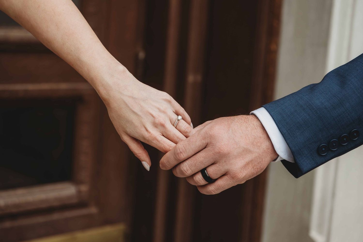 A close up image of a bride and groom holding hands, showing off their wedding rings.