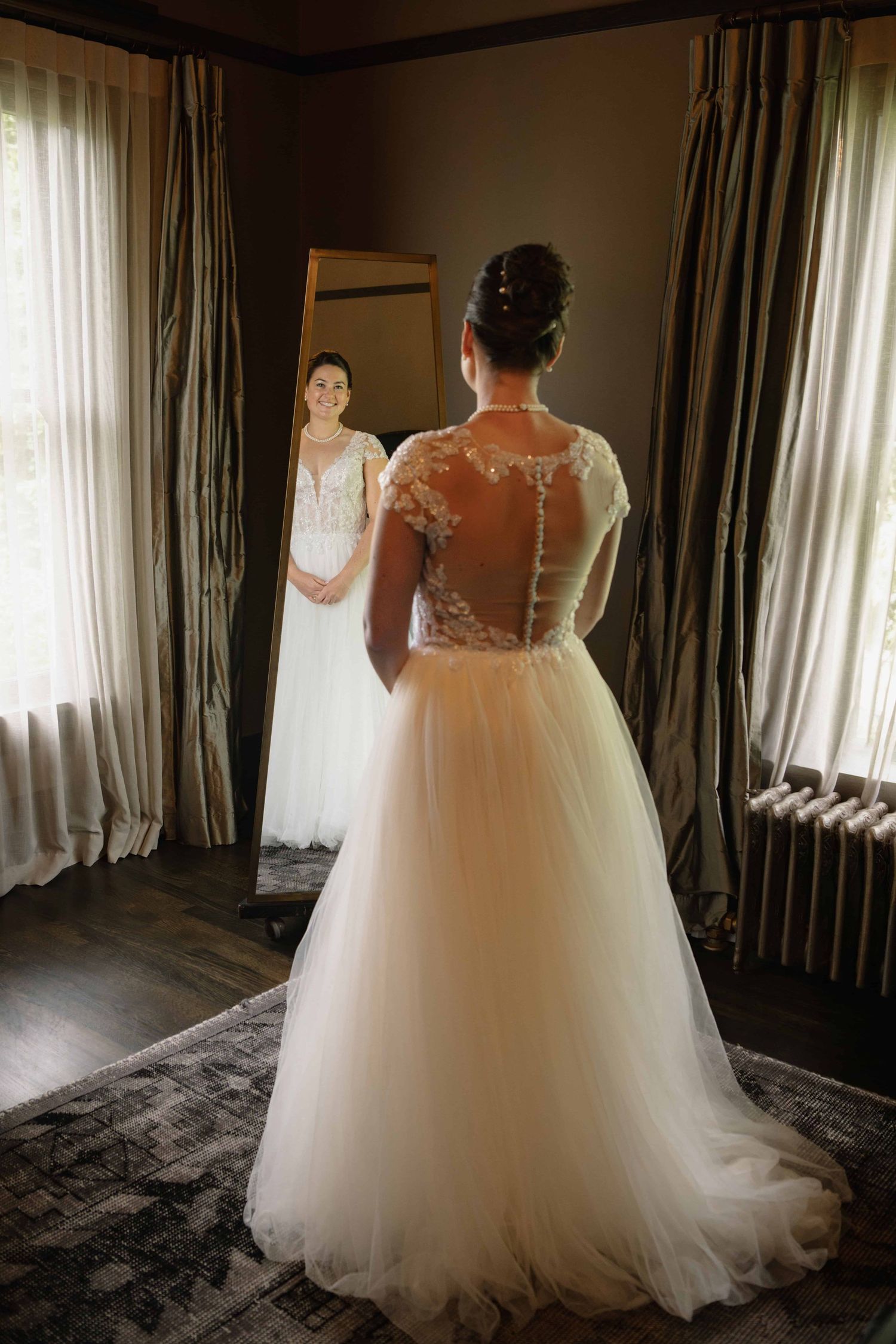 A bride in a big fluffy wedding gown looking at herself in the mirror after getting dressed.