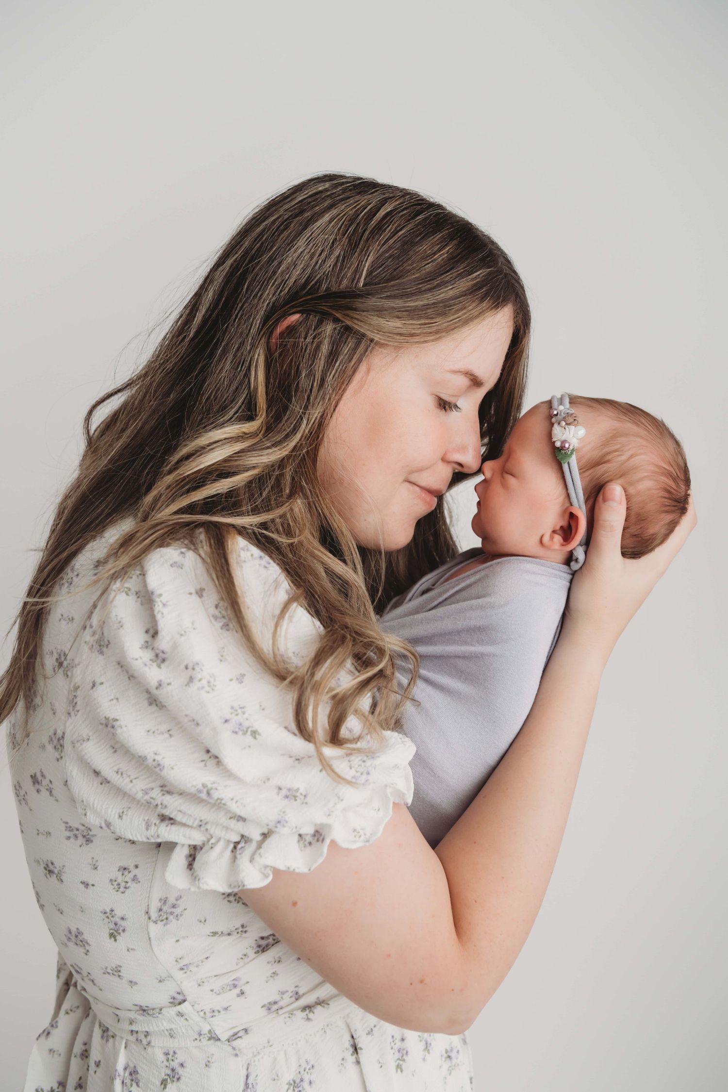A mother snuggling her newborn baby girl, wrapped in purple as she sleeps.