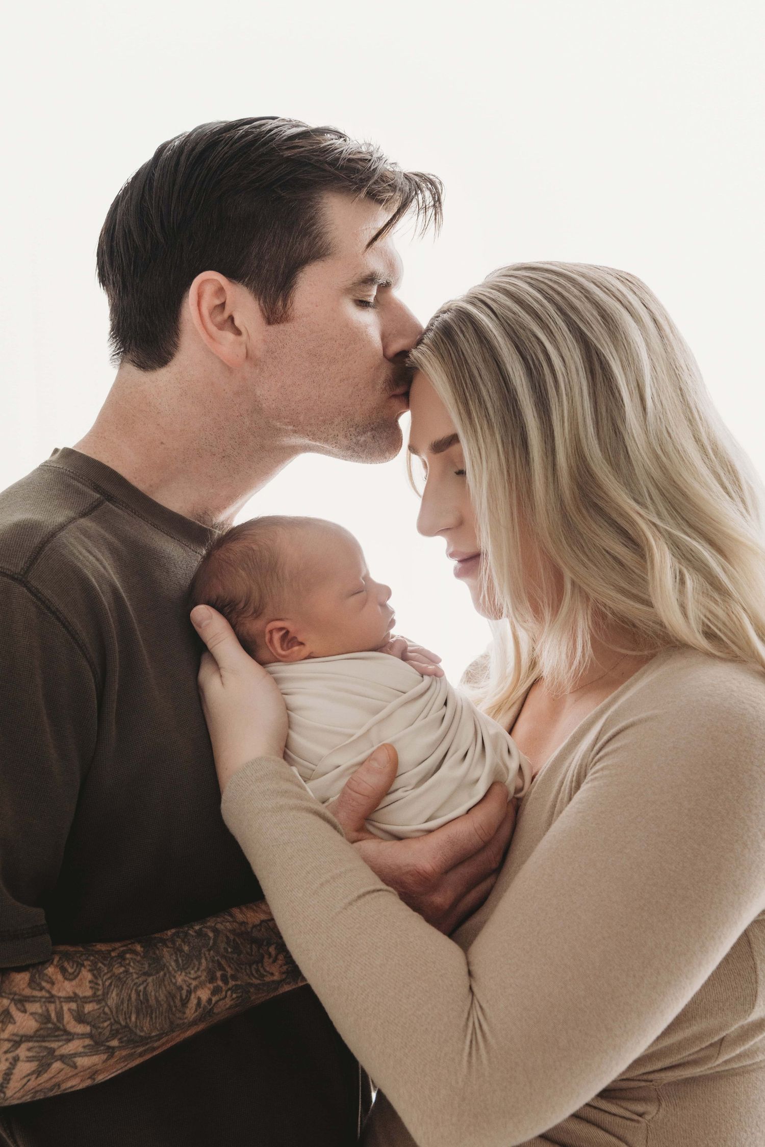 A backlit portrait of parents with their sleeping newborn.