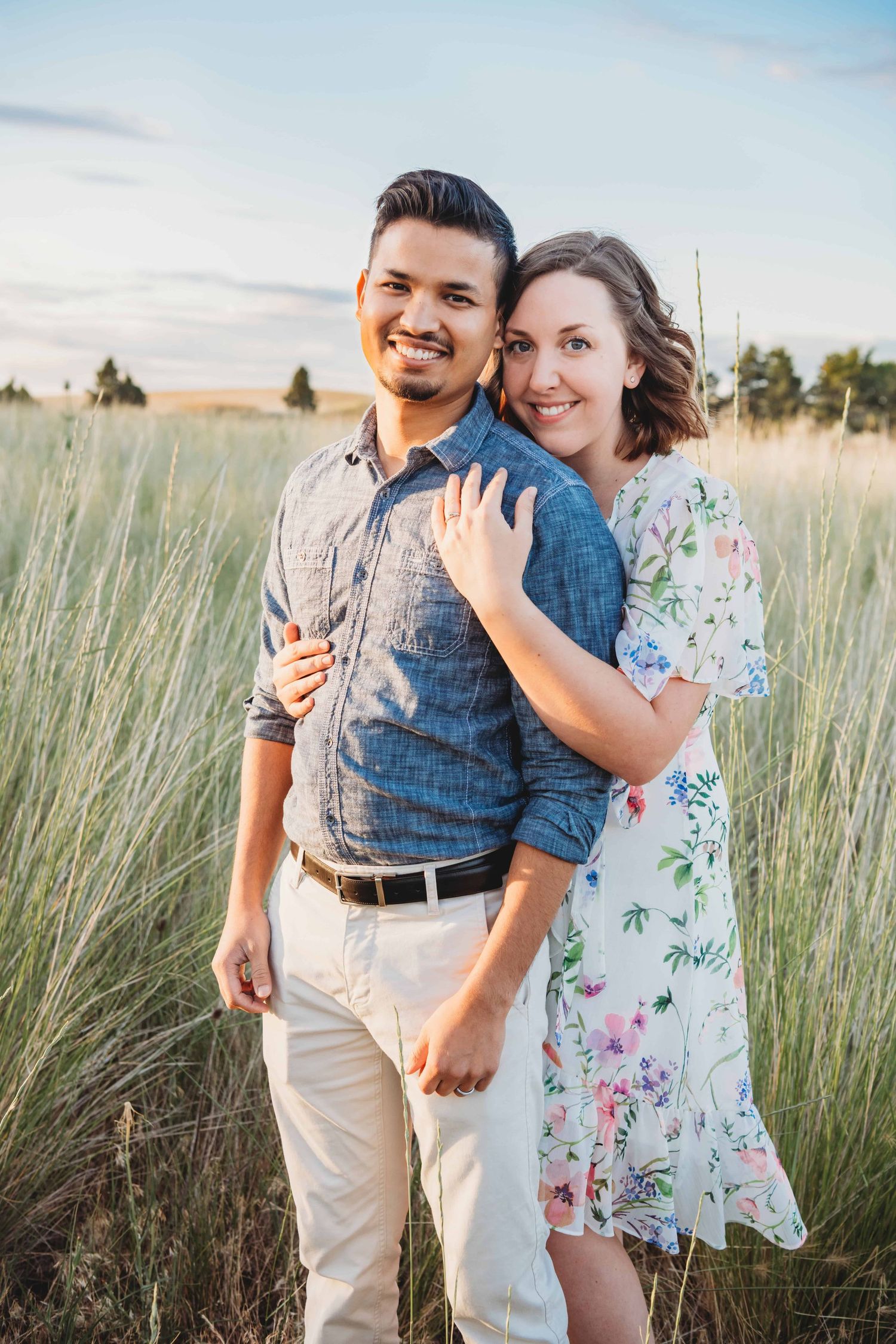 A couple standing in a green field during spring time smiling for the camera.