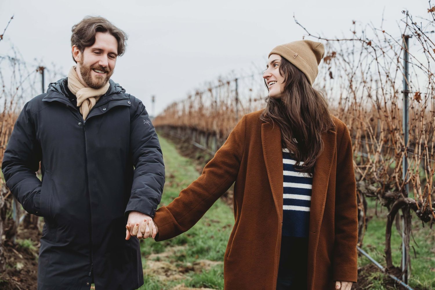 A newly engaged couple walking through a vineyard holding hands.