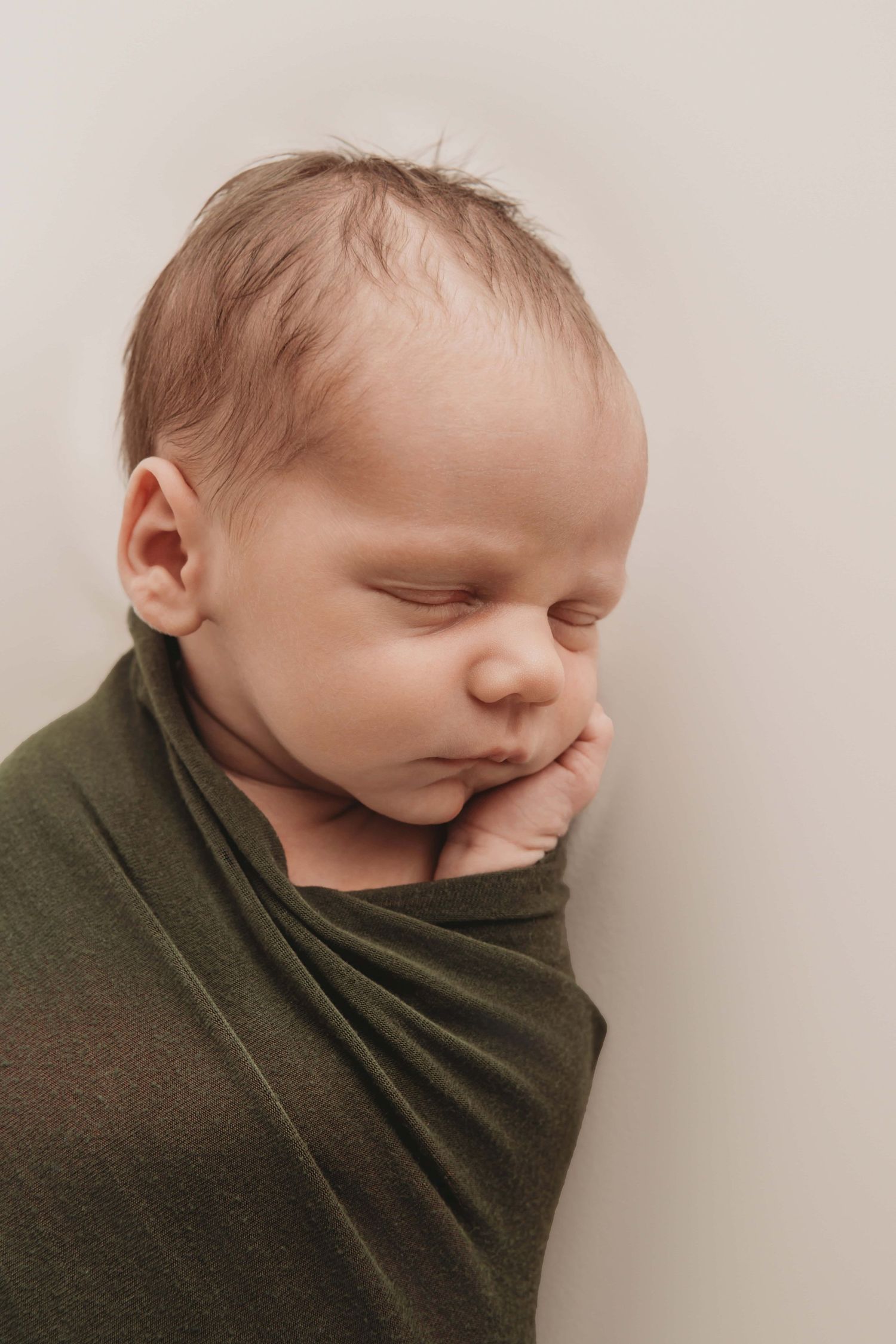 A side portrait of a sleeping newborn wrapped in dark green.