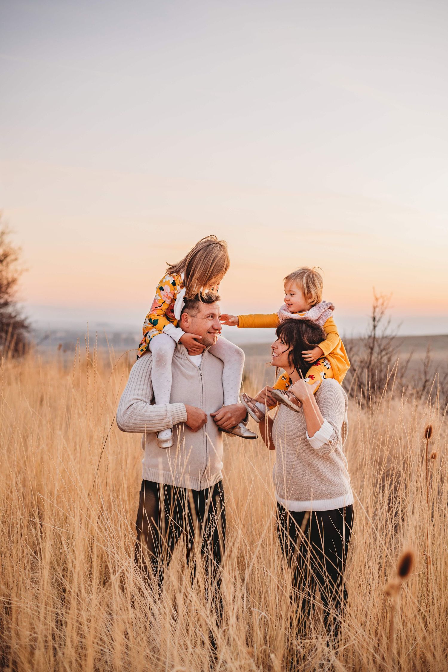 A family with two girls on their parent's shoulders during sunset in Walla Walla.