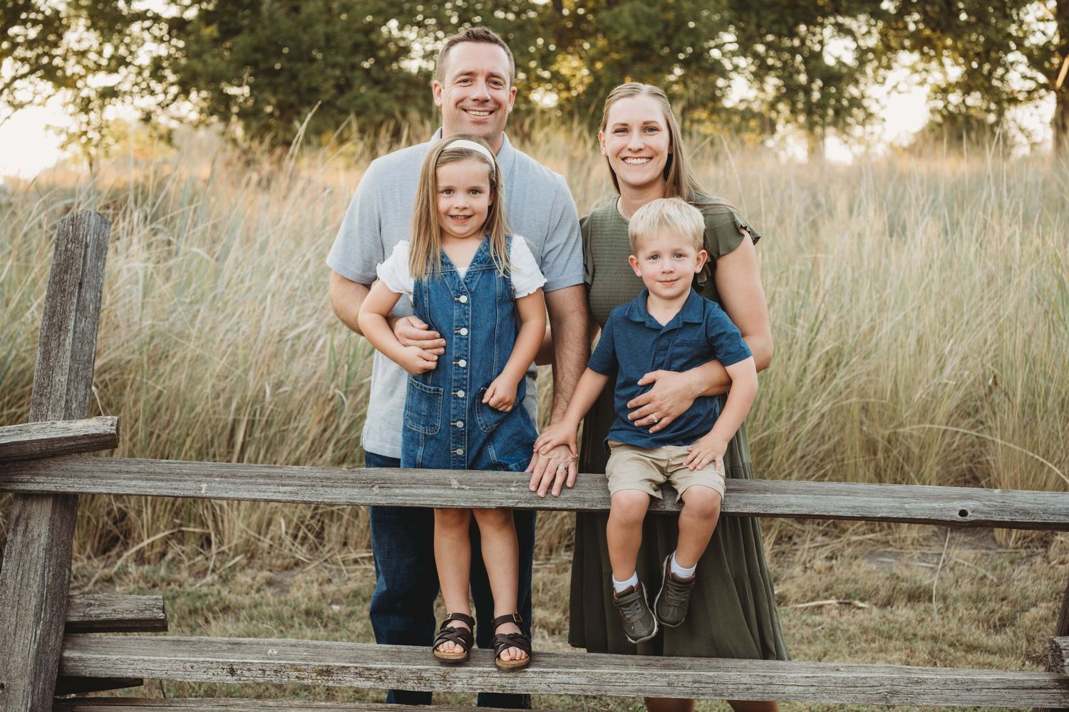 Outdoor family photography in Walla Walla featuring parents and two children standing together along a wooden fence.
