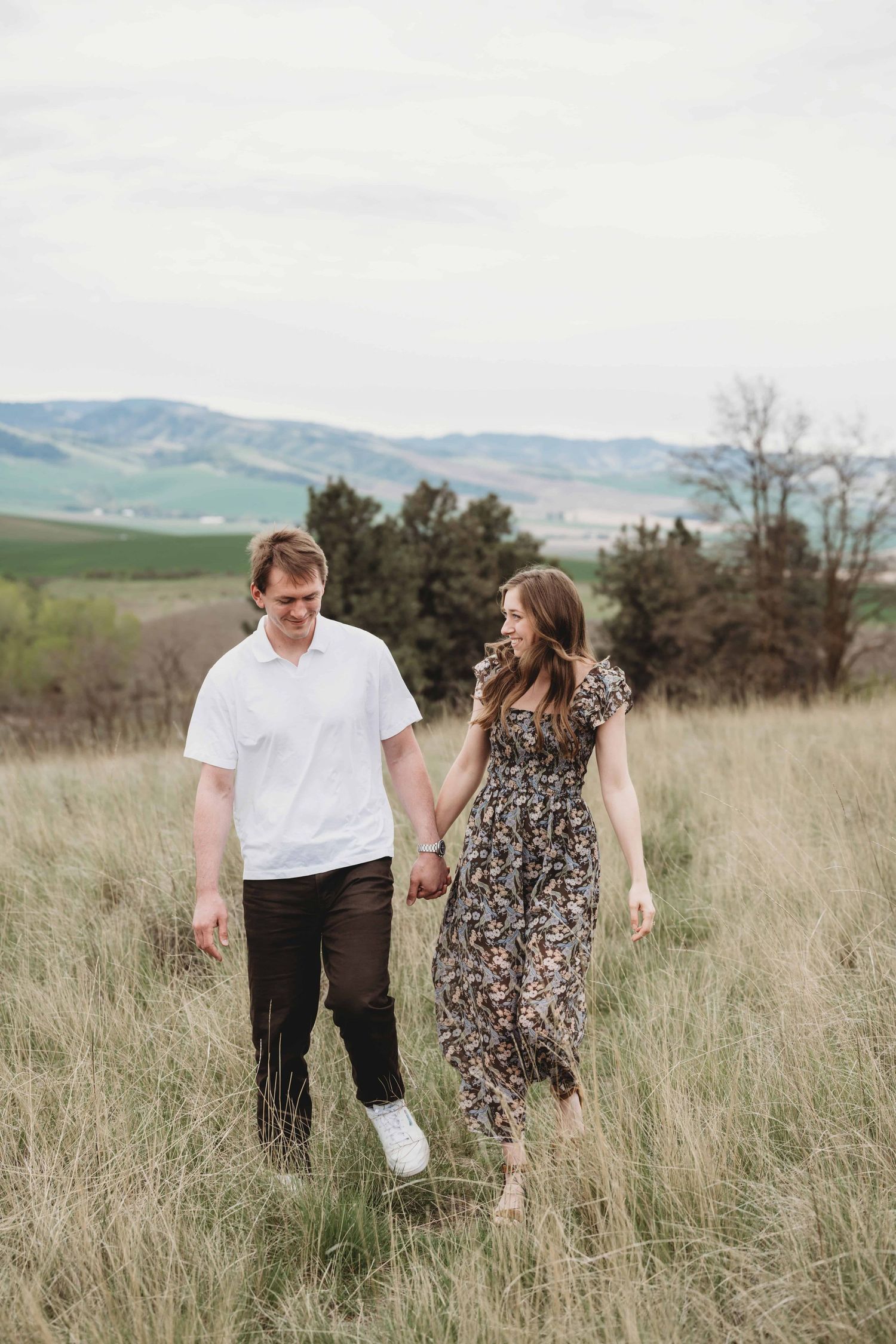 A couple walking through tall grass holding hands and laughing together.