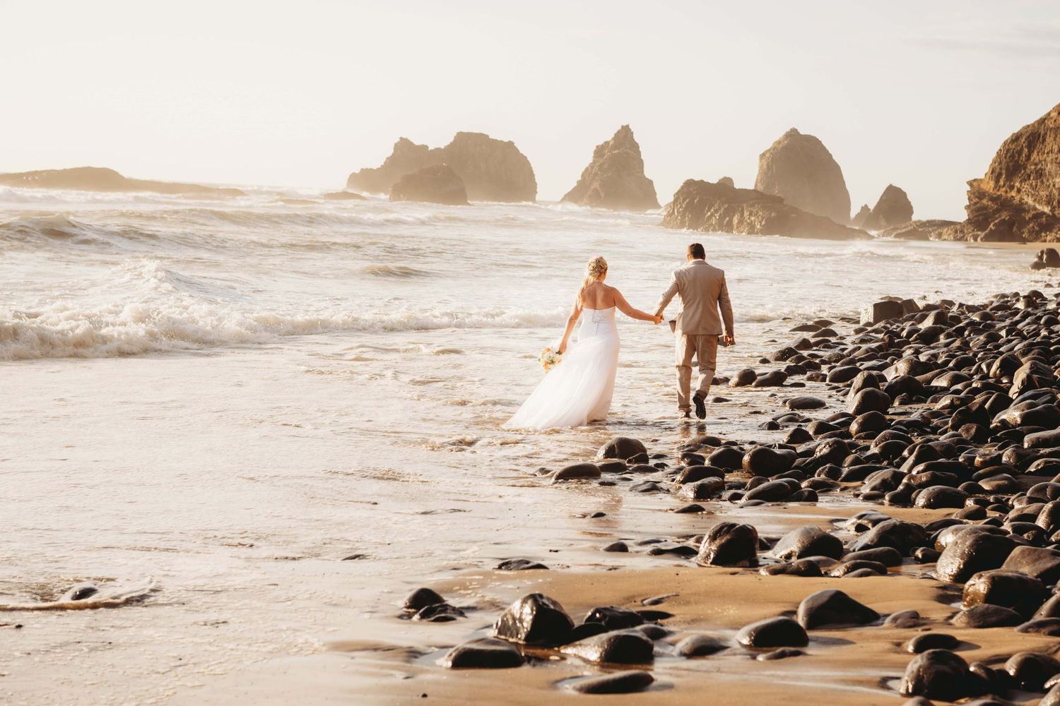 A couple walking holding hands along the shore of a beach on the Oregon coast.